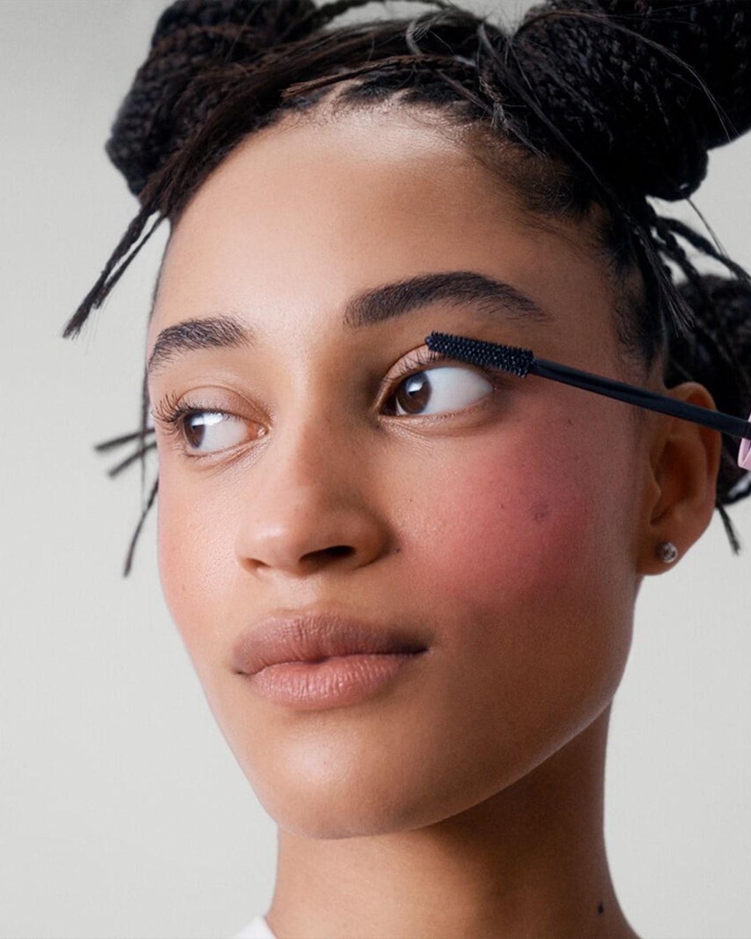 Une femme applique du mascara noir sur ses cils supérieurs avec une brosse noire, rehaussant son regard avec une touche de couleur.