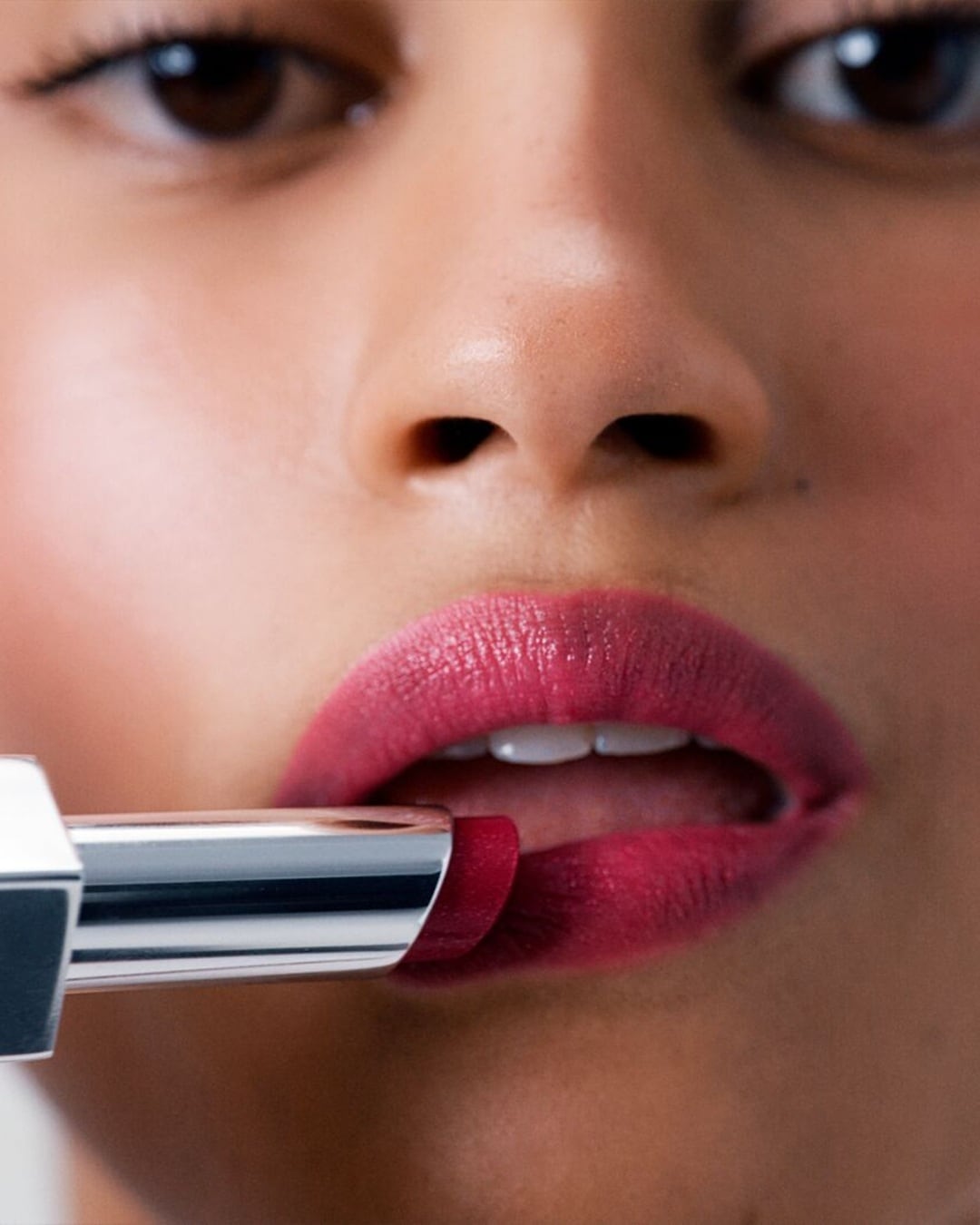 Gros plan d'une femme appliquant un rouge à lèvres rouge foncé brillant avec un tube argenté, mettant en valeur la couleur riche et la texture crémeuse.
