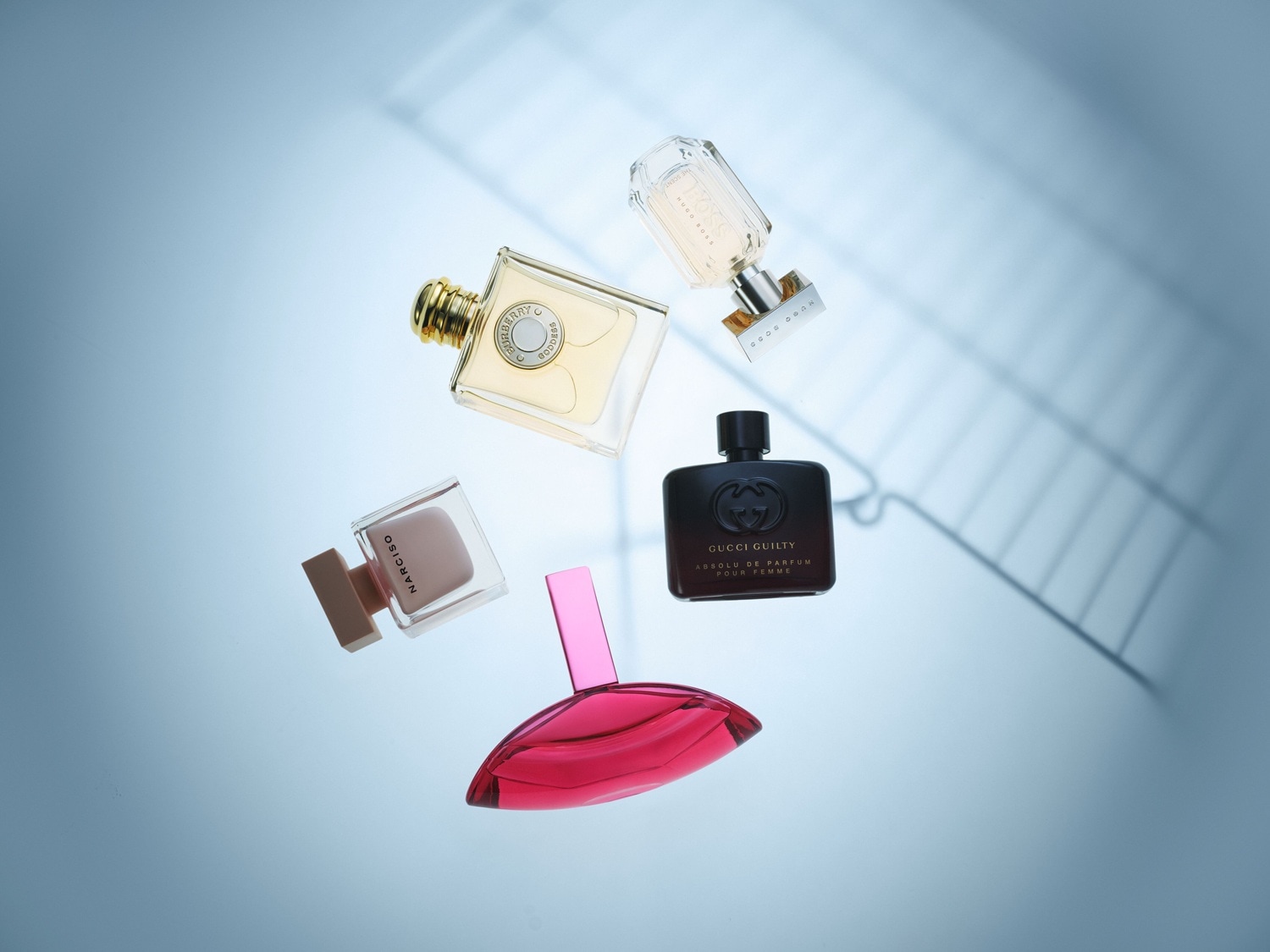 Verschiedene Parfümflakons von Gucci Guilty, Hugo Boss, Narciso und anderen Marken schweben auf hellblauem Hintergrund.