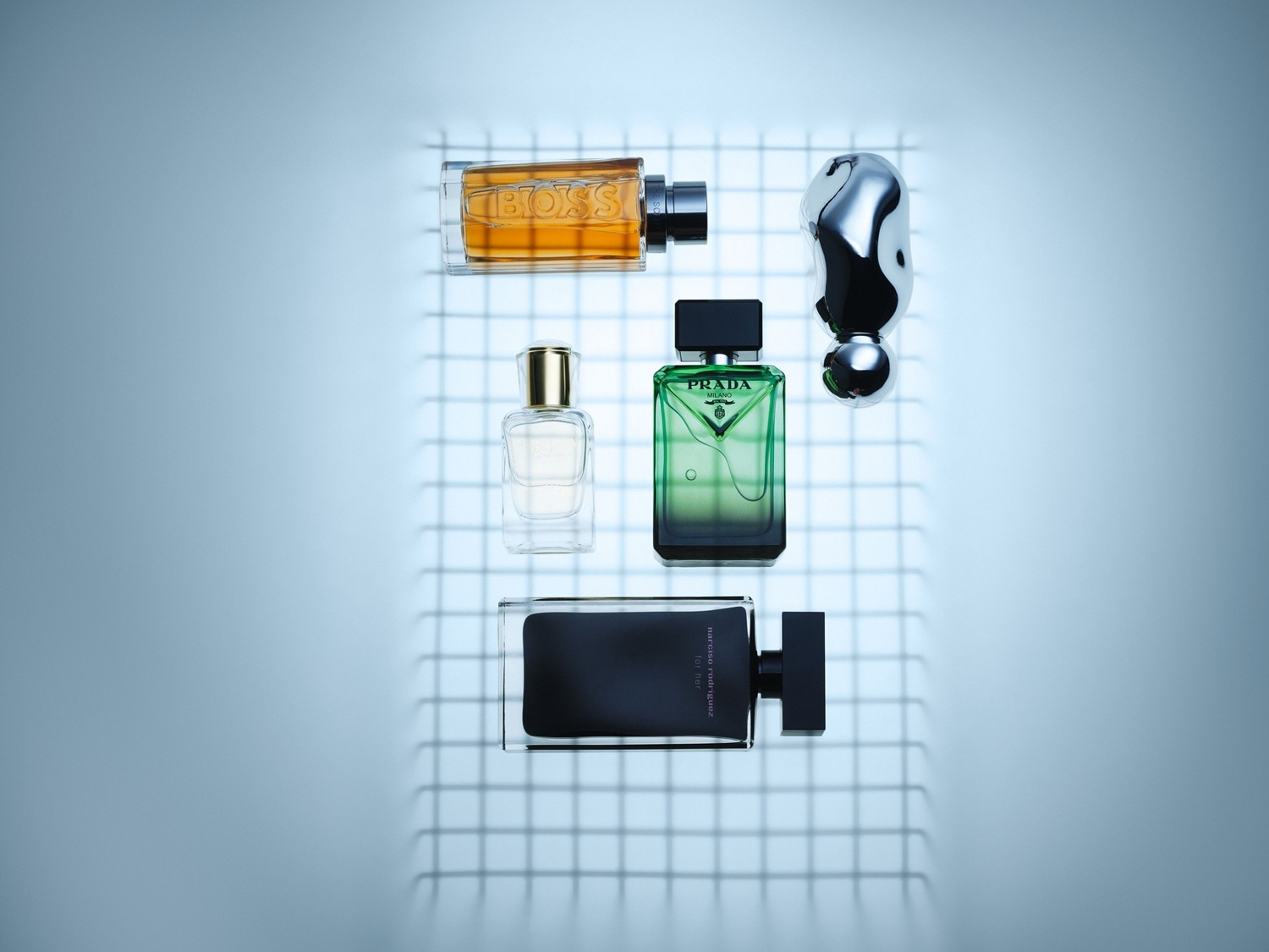 Verschiedene Parfümflakons von Boss, Prada und Narciso Rodriguez sind auf einem hellblauen Hintergrund mit einem Gittermuster angeordnet.