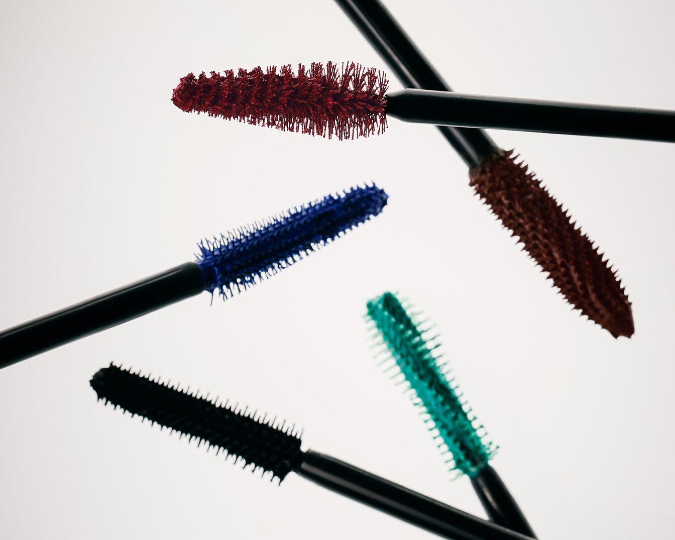 Ontdek een reeks kleurrijke mascaraborstels in rood, blauw, bruin, groen en zwart, elk met een unieke borstelvorm voor verschillende wimperlooks.