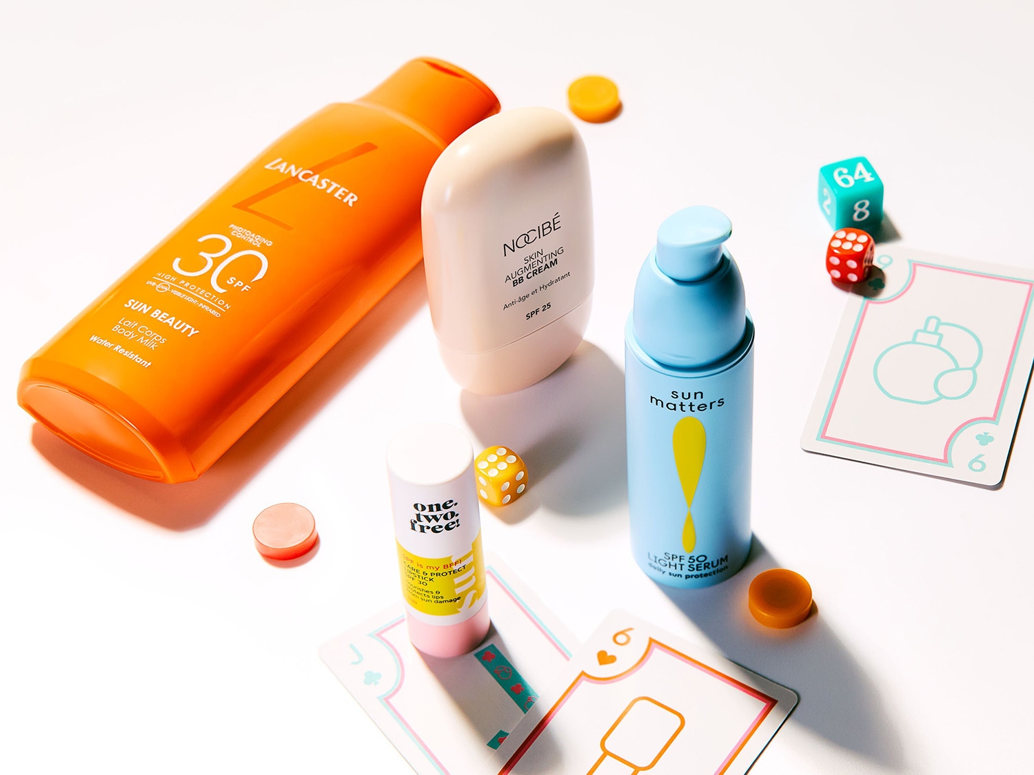 Découvrez une gamme de produits de protection solaire, incluant le lait corporel Lancaster Sun Beauty SPF 30, la BB crème Nocibé Skin Augmenting SPF 25 et le sérum léger Sun Matters SPF 50, présentés avec des dés et des cartes.