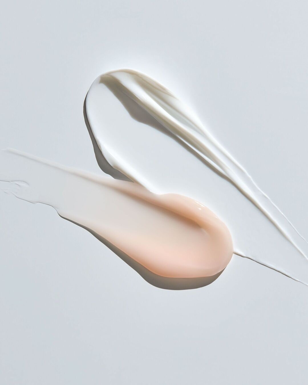 Gros plan sur des échantillons de crème blanche et rose pâle, offrant un aperçu de leur texture lisse et hydratante.