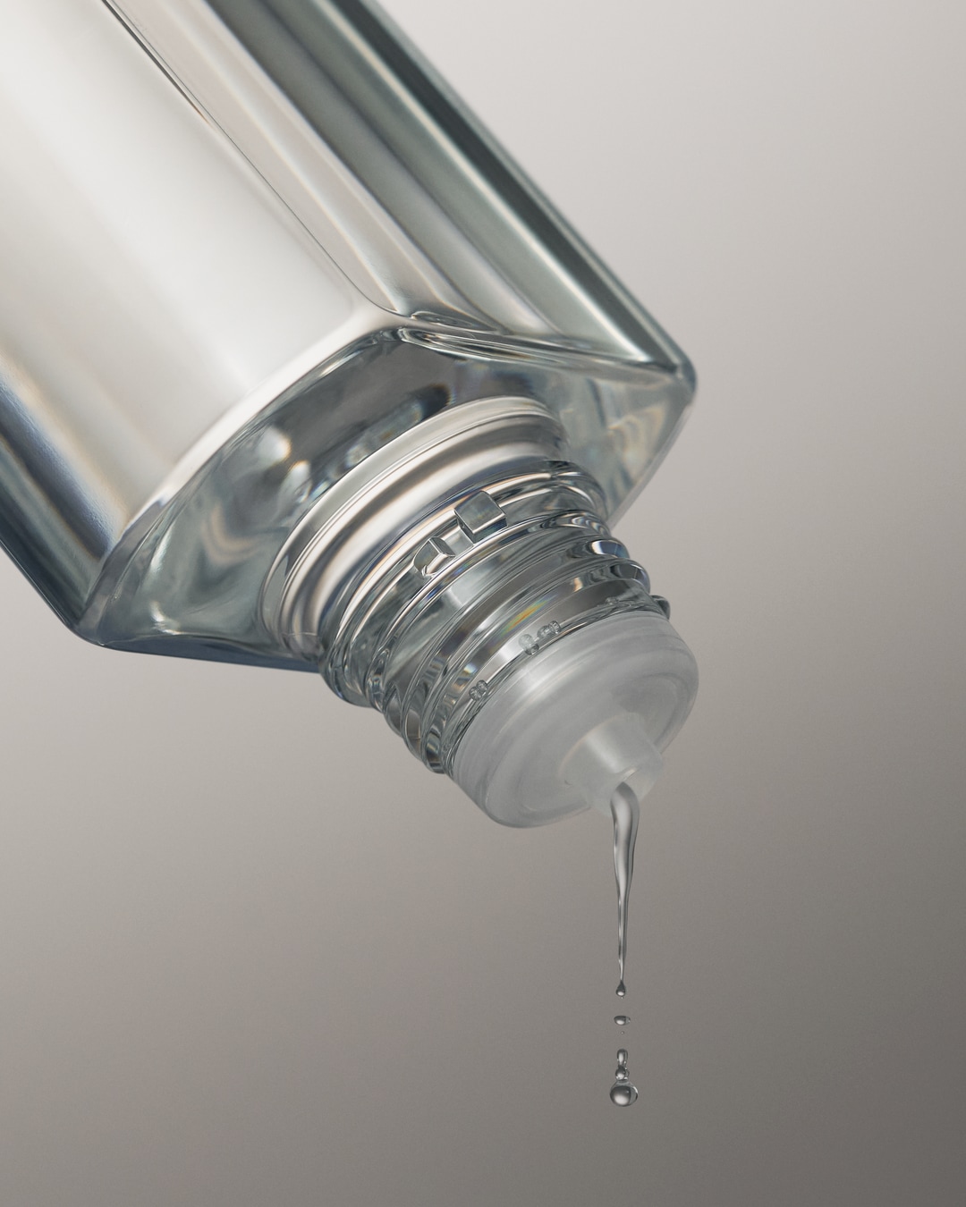 Gros plan d'un flacon transparent renversé, laissant échapper des gouttes d'un liquide clair, évoquant la pureté et l'hydratation.