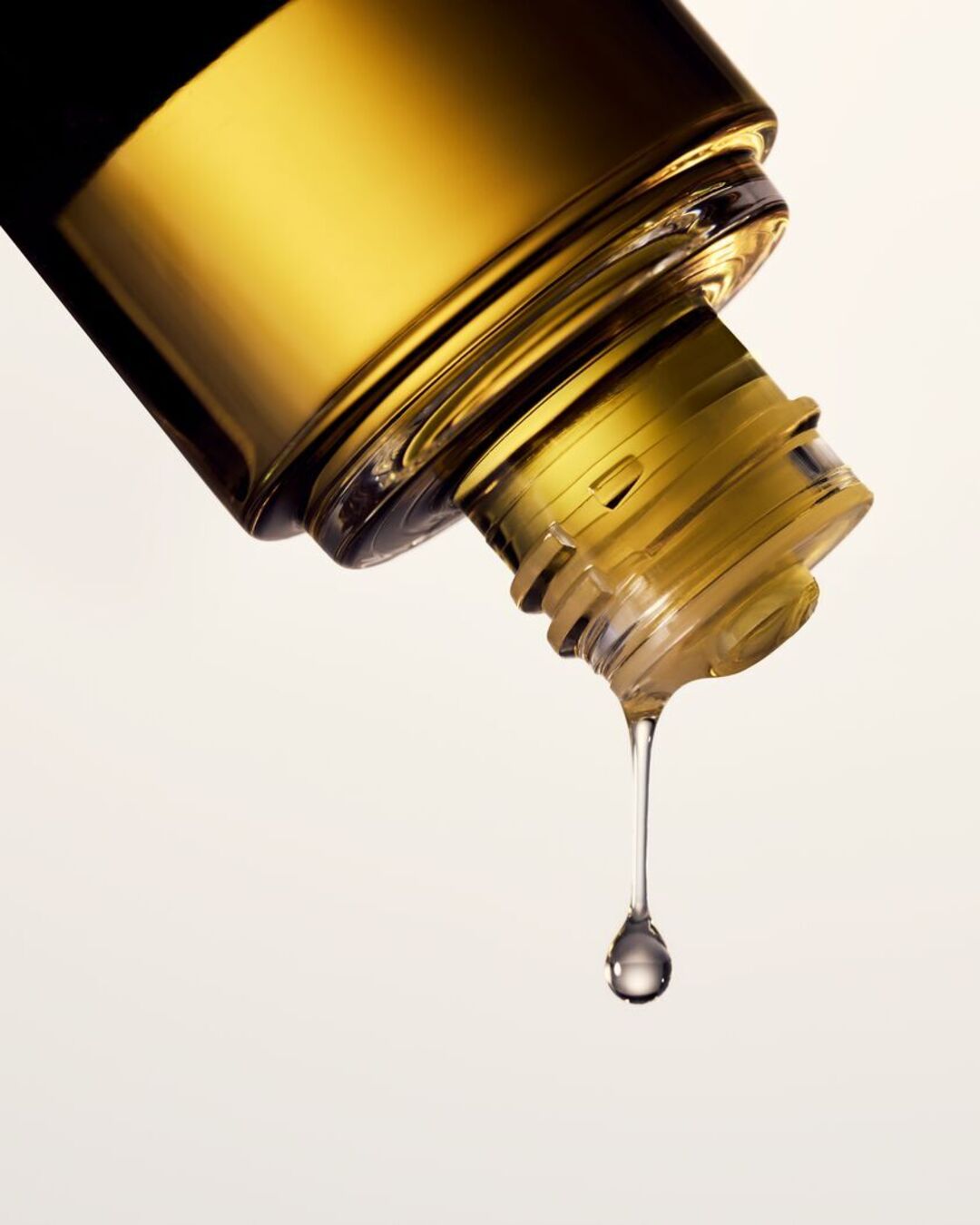 Gros plan sur un flacon d'huile dorée renversé, une goutte translucide perle, évoquant la pureté et l'éclat du soin.
