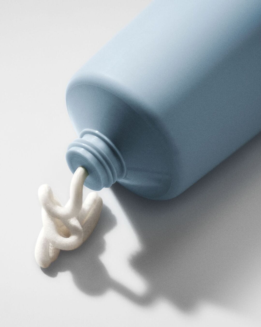 Voici un tube bleu pastel duquel sort une crème blanche, offrant un aperçu de sa texture onctueuse et hydratante.