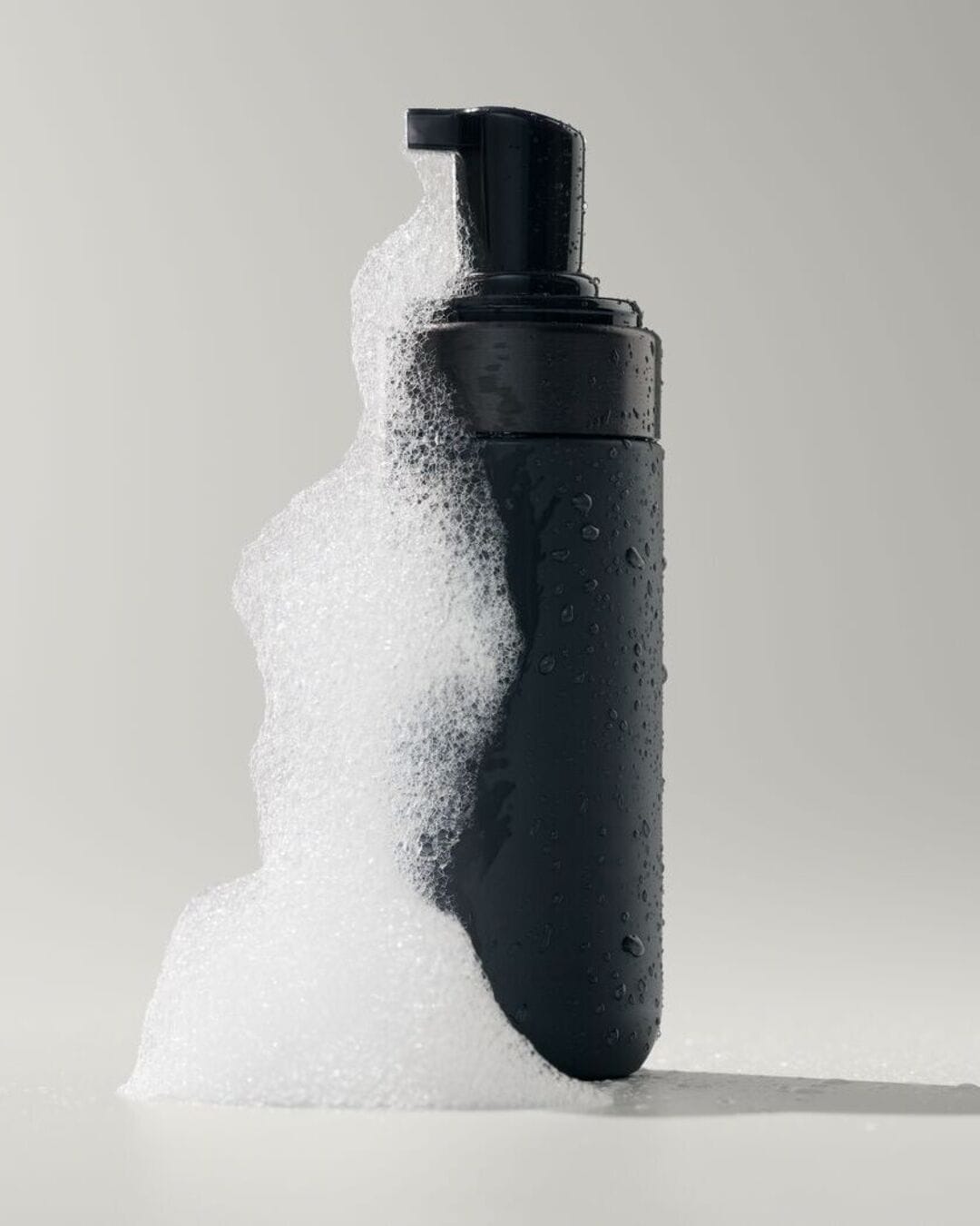 Voici un flacon noir de nettoyant moussant, entouré d'une mousse blanche et légère, parfait pour une peau propre et fraîche.