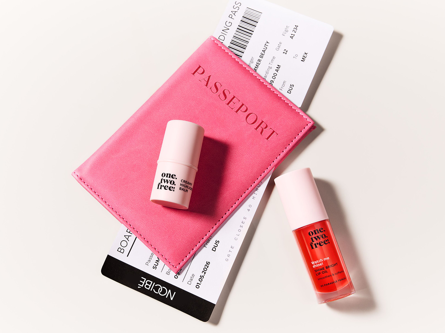 Un passeport rose, un baume en stick et une huile à lèvres corail de One.Two.Free, présentés avec un billet d'avion pour un look beauté prêt pour le voyage.