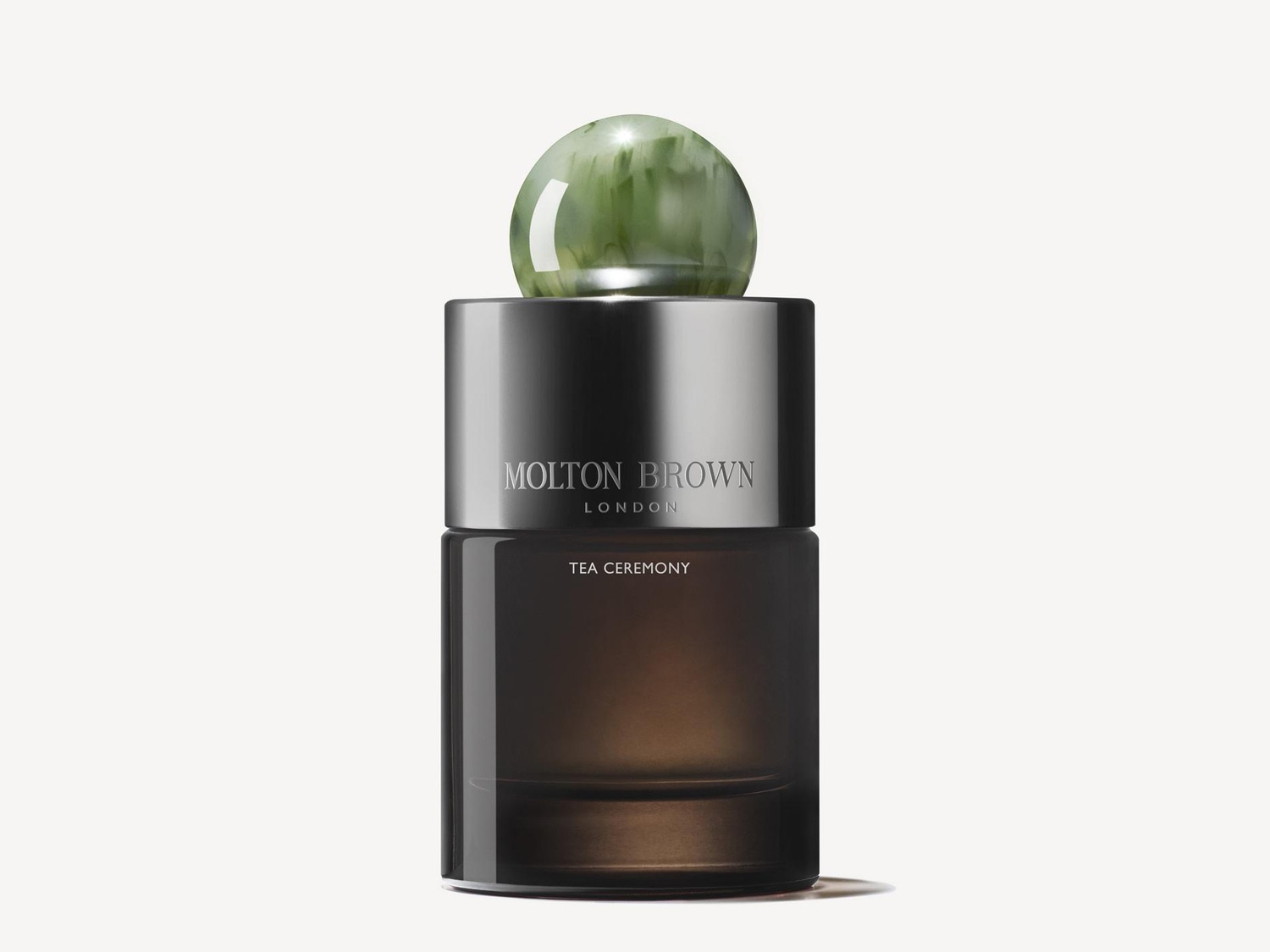 Flakón Molton Brown London Tea Ceremony má hnedé sklo, strieborný vrchnák a zelenú guľovú zátku.