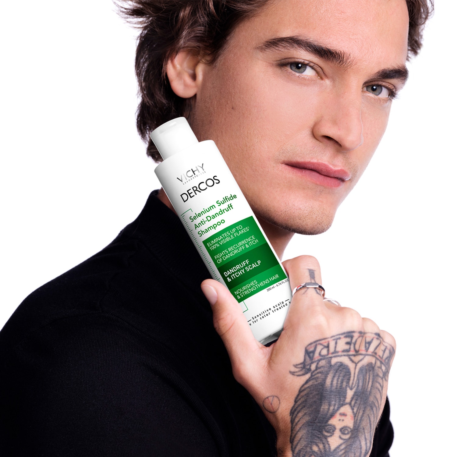 Un homme tient un flacon blanc de shampooing antipelliculaire Vichy Dercos Selenium Sulfide, qui promet d'éliminer jusqu'à 100 % des pellicules visibles et de nourrir le cuir chevelu.