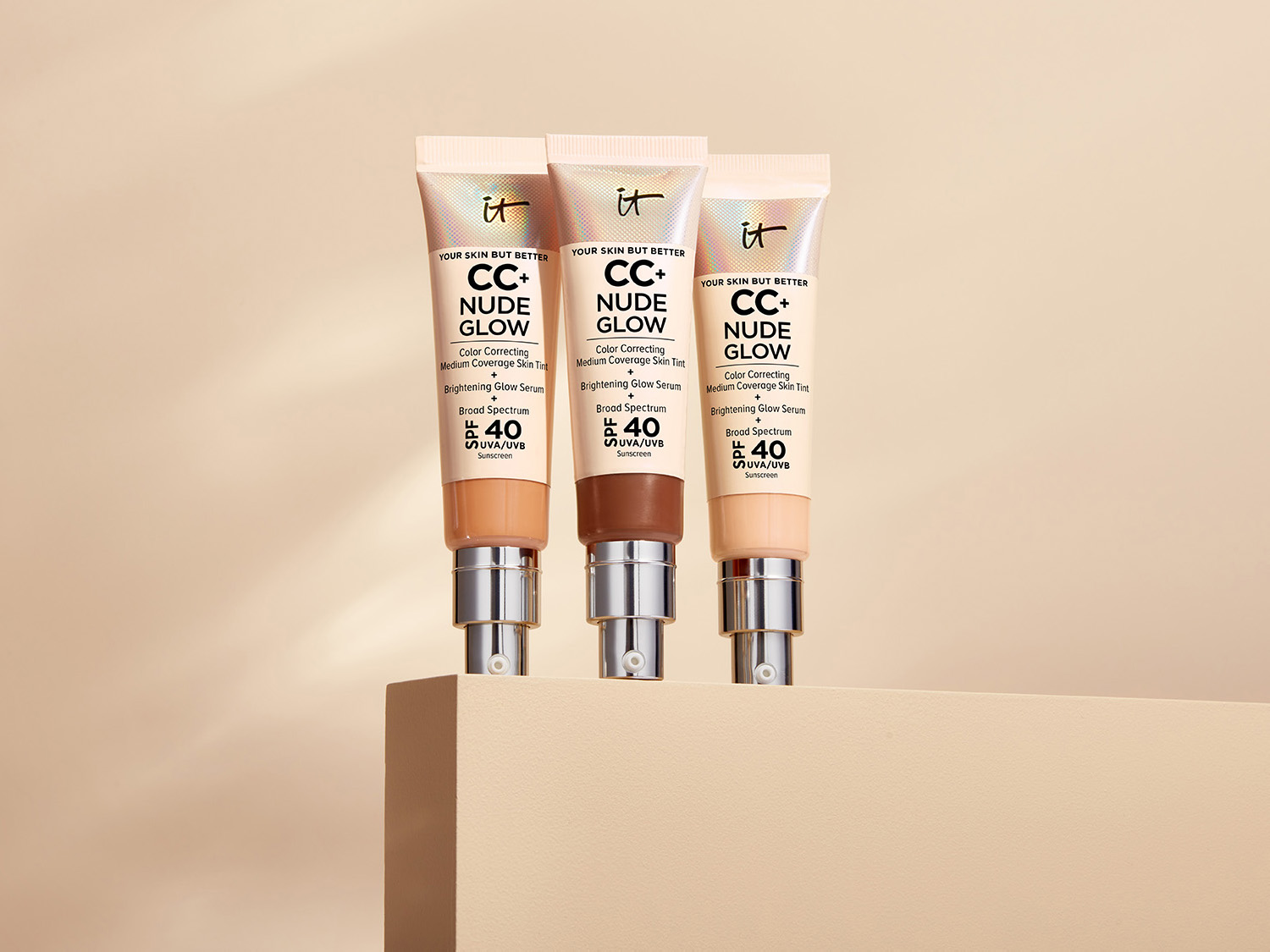 Trzy tubki kremu CC+ Nude Glow od IT Cosmetics w odcieniach beżu i brązu, obiecujące korekcję koloru, średnie krycie i rozświetlenie, z filtrem SPF 40.