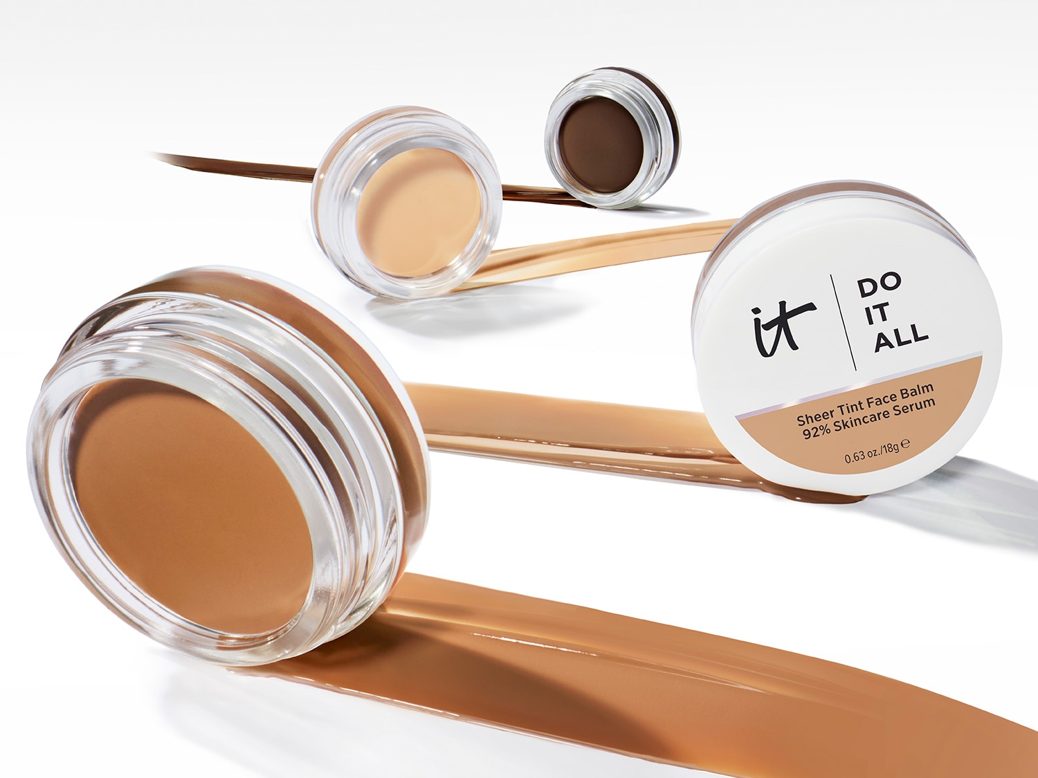 Balsam do twarzy It Cosmetics Sheer Tint Face Balm 92% Skincare Serum w okrągłym słoiczku z przezroczystą nakrętką, obok niego rozmazana próbka balsamu.