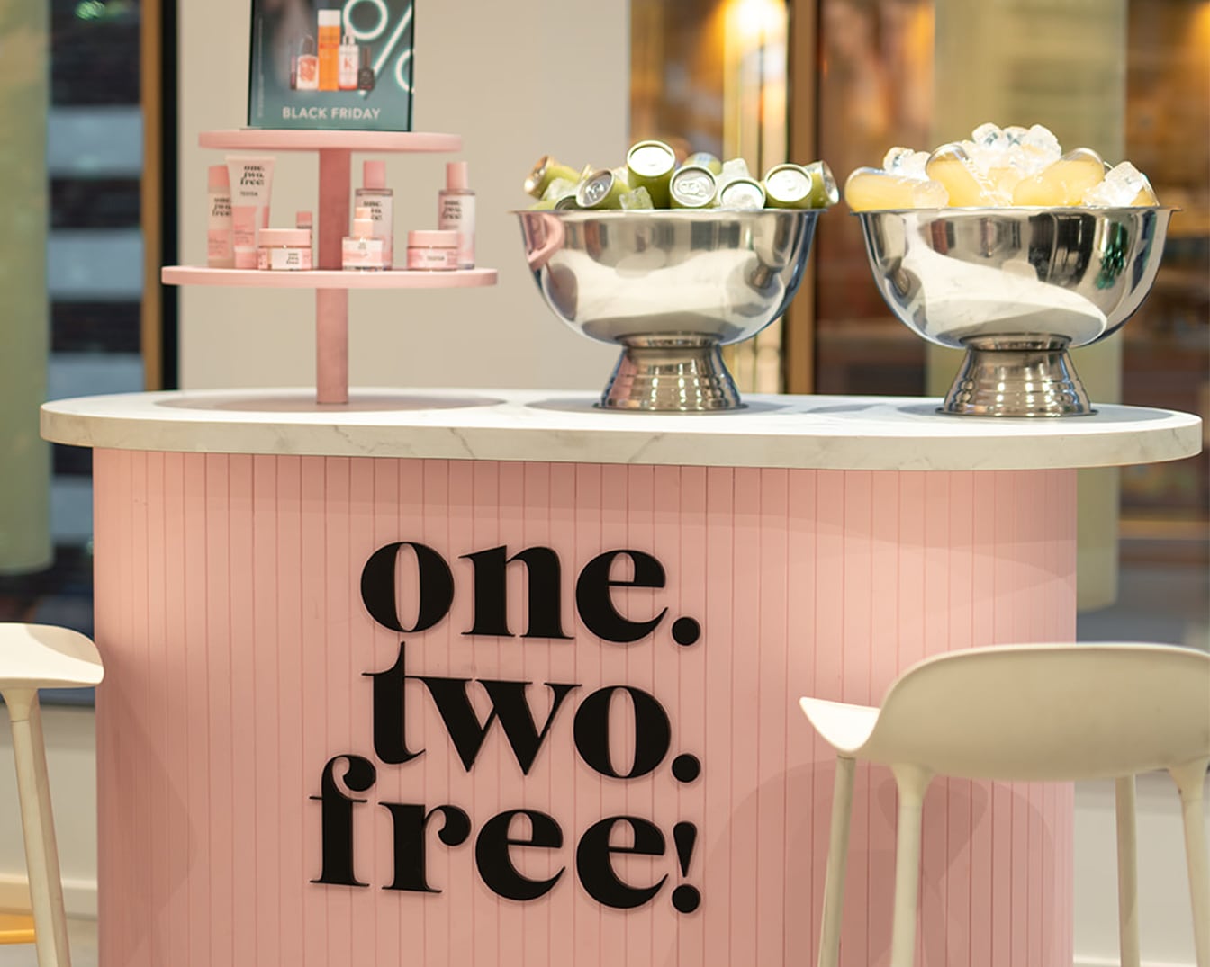 Roze bar met de tekst 'one. two. free!' erop, met zilveren kommen gevuld met ijs en drankjes, en een etagère met huidverzorgingsproducten.