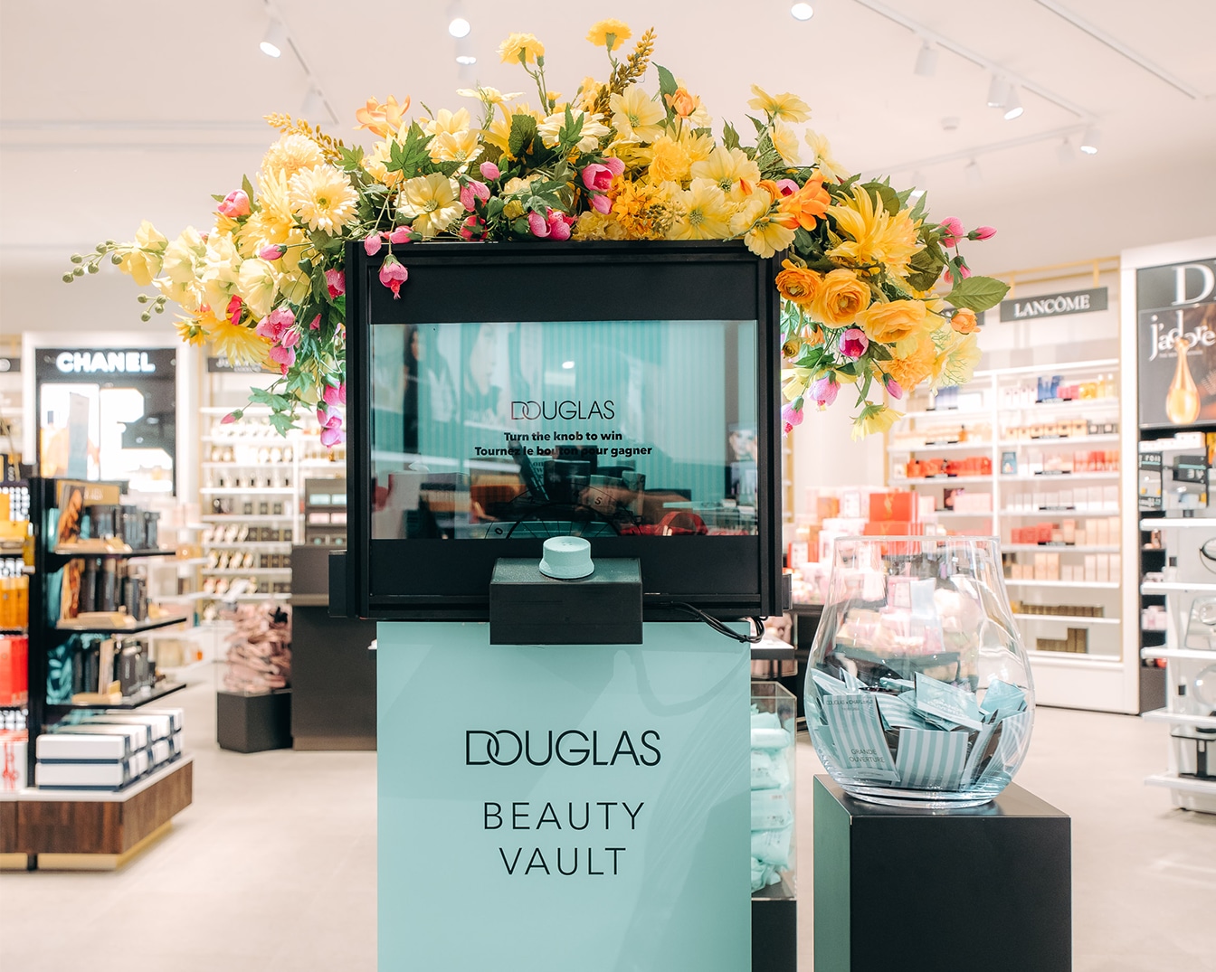 Een Douglas Beauty Vault met een scherm omringd door gele en roze bloemen, met de tekst 'Turn the knob to win'.