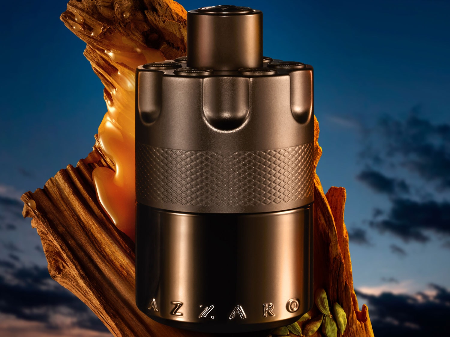 Butelka Azzaro w kształcie rewolweru, wykonana z ciemnego metalu, stoi na tle kawałka drewna z kroplami bursztynowego płynu, co dodaje jej tajemniczości i męskiego charakteru.