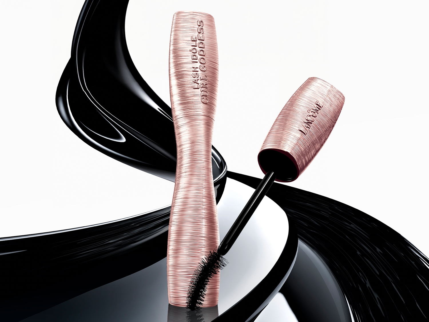 Maskara Lancôme Lash Idôle Curl Goddess w metalicznym, różowo-złotym opakowaniu z czarną szczoteczką na tle abstrakcyjnej, czarnej plamy.