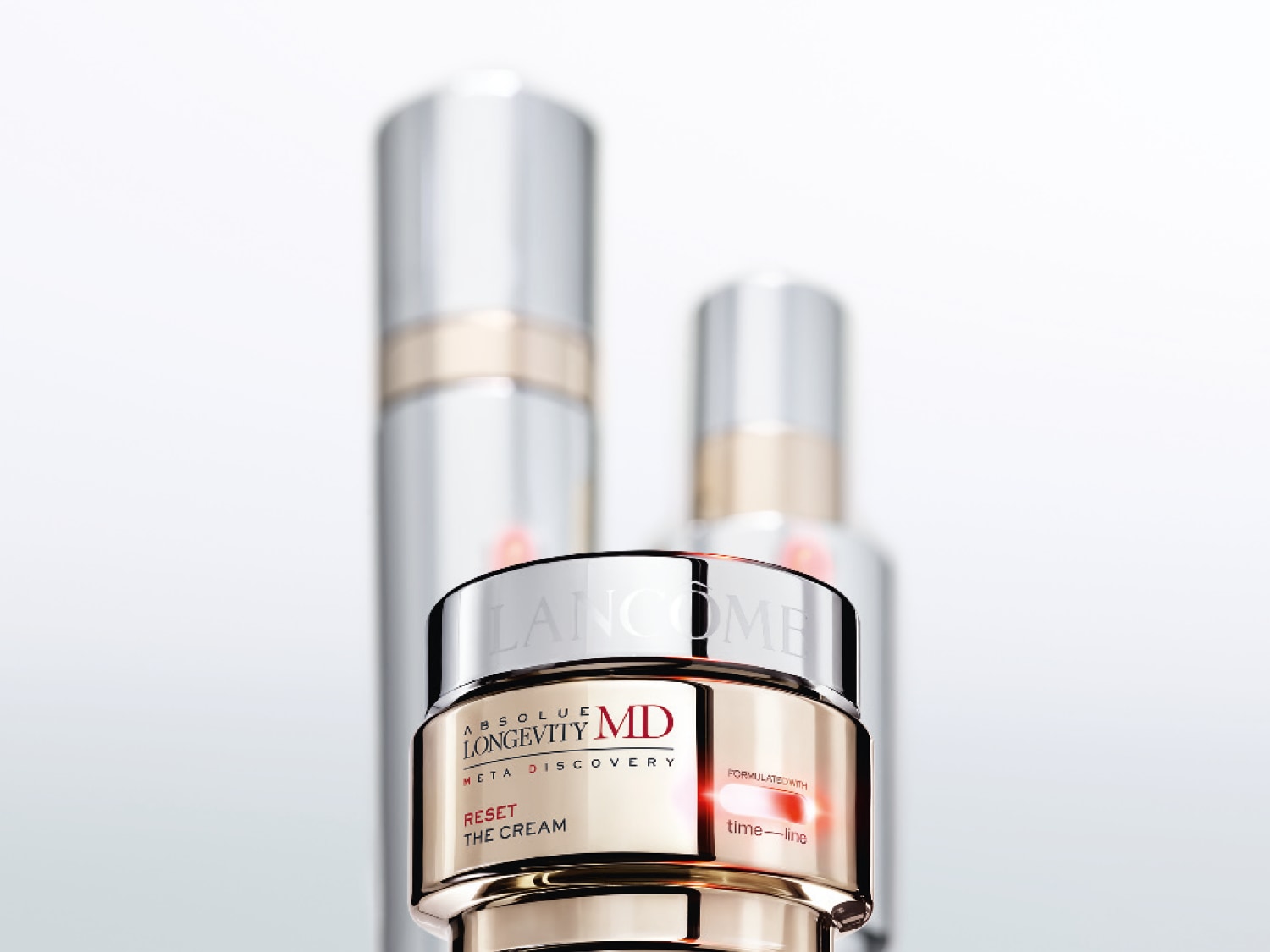 Krem Lancôme Absolue Longevity MD Meta Discovery Reset The Cream w złotym słoiczku z srebrną nakrętką, obok rozmyte srebrne butelki.