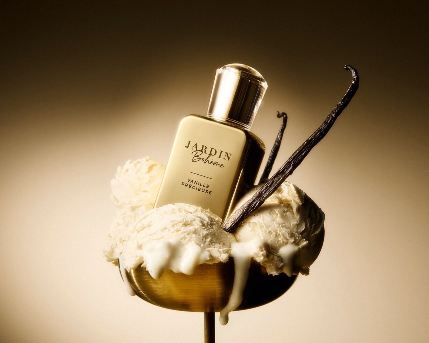 Perfumy Jardin Bohème Vanille Précieuse w złotym flakonie, otoczone gałkami lodów waniliowych i laskami wanilii, tworzą luksusową kompozycję zapachową.