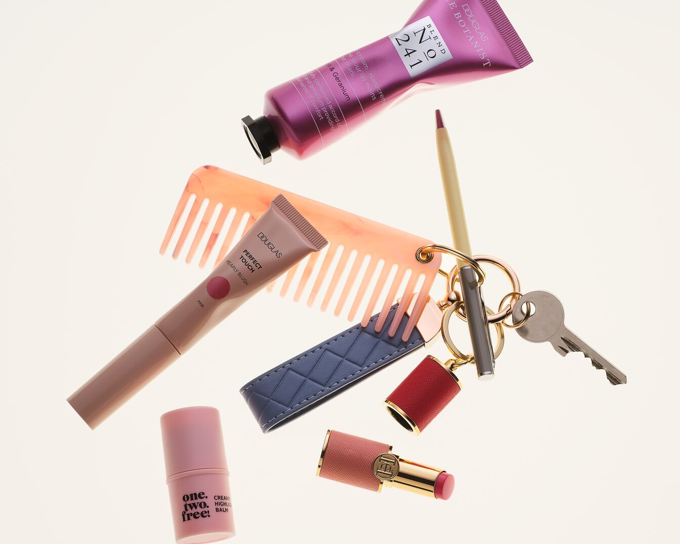 Verschiedene Beauty-Produkte von Douglas, darunter Handcreme, Rouge, Lippenstift und ein Kamm, sind auf einem Schlüsselbund befestigt.