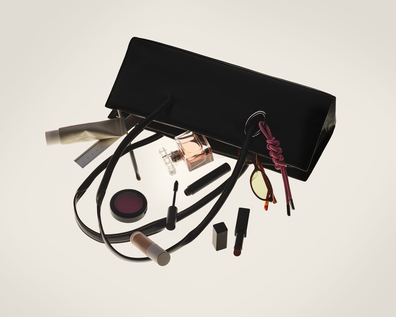 Schwarze Handtasche mit Kosmetika wie Parfüm, Mascara, Lippenstift und Sonnenbrille, die einen Einblick in die Must-haves für unterwegs gibt.