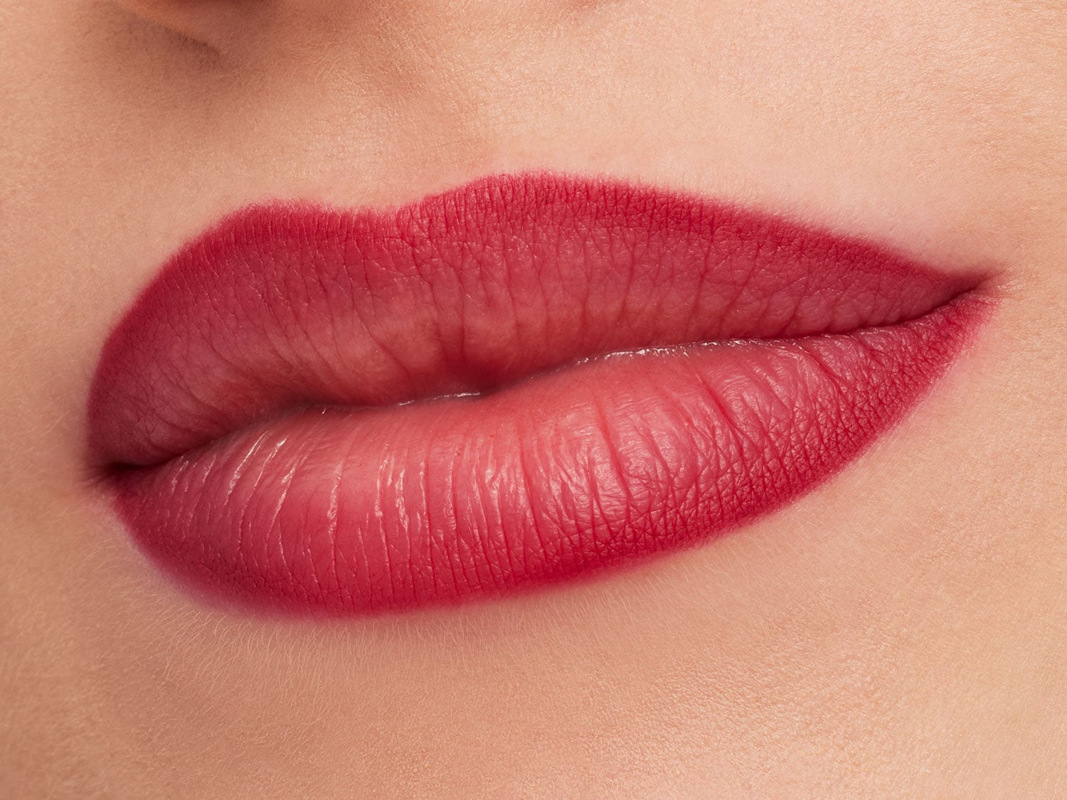 Close-up van lippen met een rode ombre lippenstift, waarbij de kleur geleidelijk overgaat van donkerrood naar een lichtere tint.