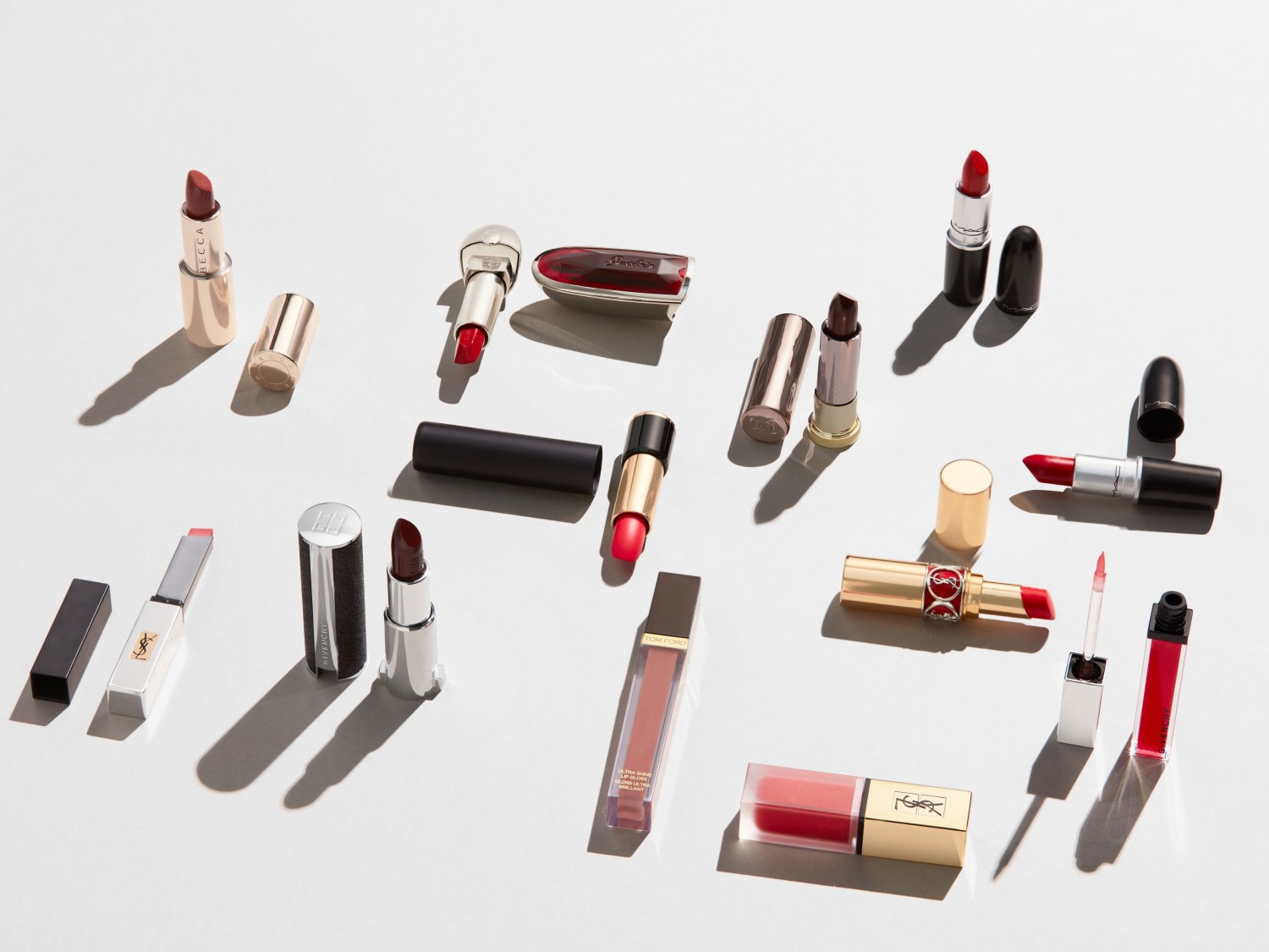 O varietate de rujuri și gloss-uri de buze de la mărci precum YSL, MAC și Givenchy, prezentate în tuburi elegante aurii, negre și argintii, cu nuanțe de roșu intens și tonuri nude.