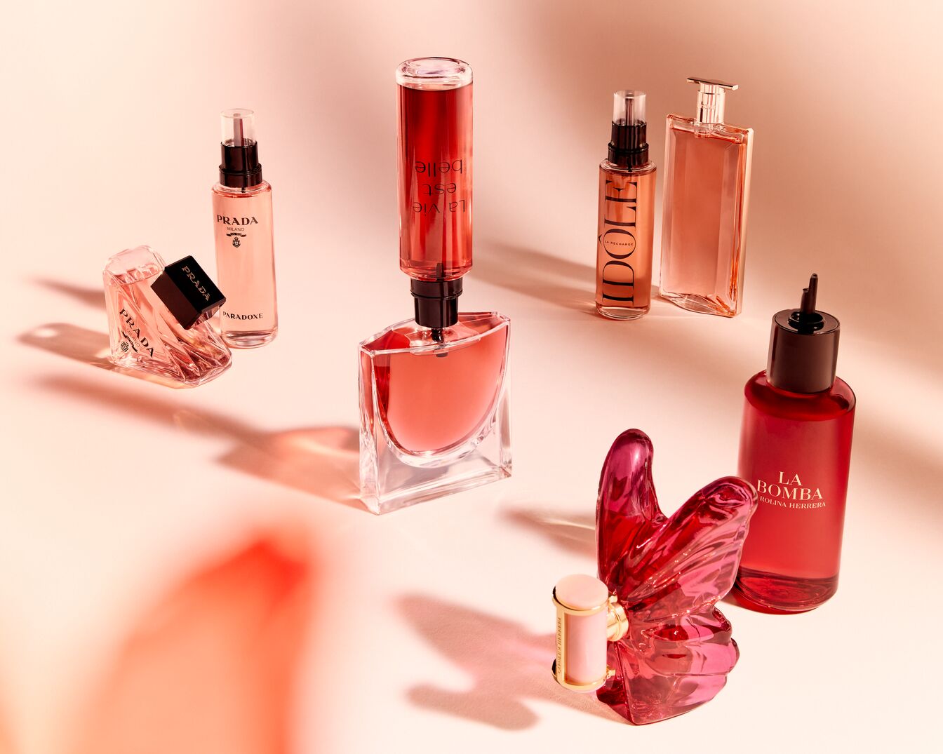 Découvrez une collection de parfums de luxe, incluant Prada Paradoxe, La Vie Est Belle, Idôle et La Bomba, présentés dans des flacons élégants aux teintes roses et rouges.