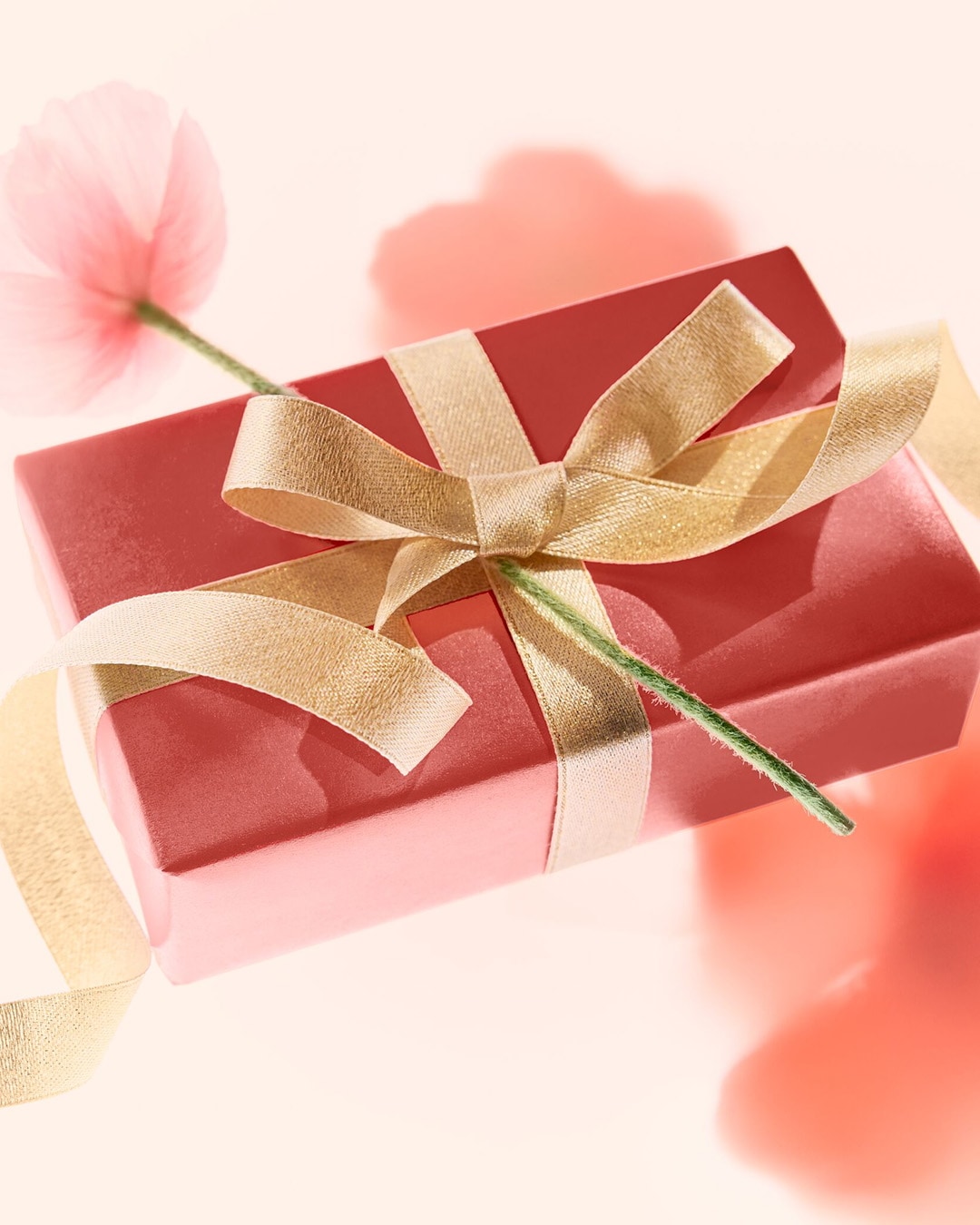Boîte cadeau rouge ornée d'un ruban doré et d'une fleur rose, parfaite pour offrir un moment de bonheur.