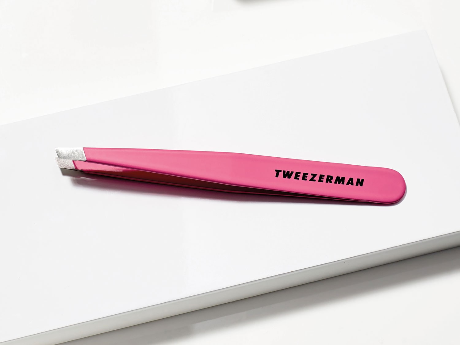 Nahaufnahme einer pinkfarbenen Pinzette der Marke Tweezerma, die auf einer weißen Oberfläche liegt.