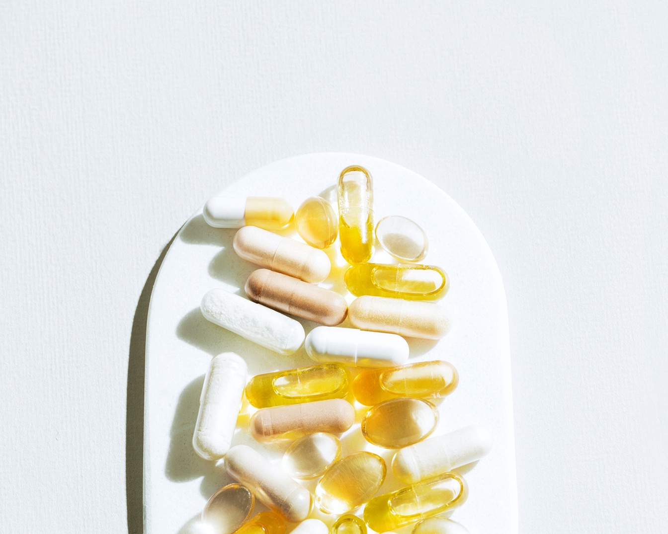 Verschiedene Nahrungsergänzungsmittel, darunter weiße, hellbraune und gelbe Kapseln und Pillen, liegen auf einer weißen Oberfläche.