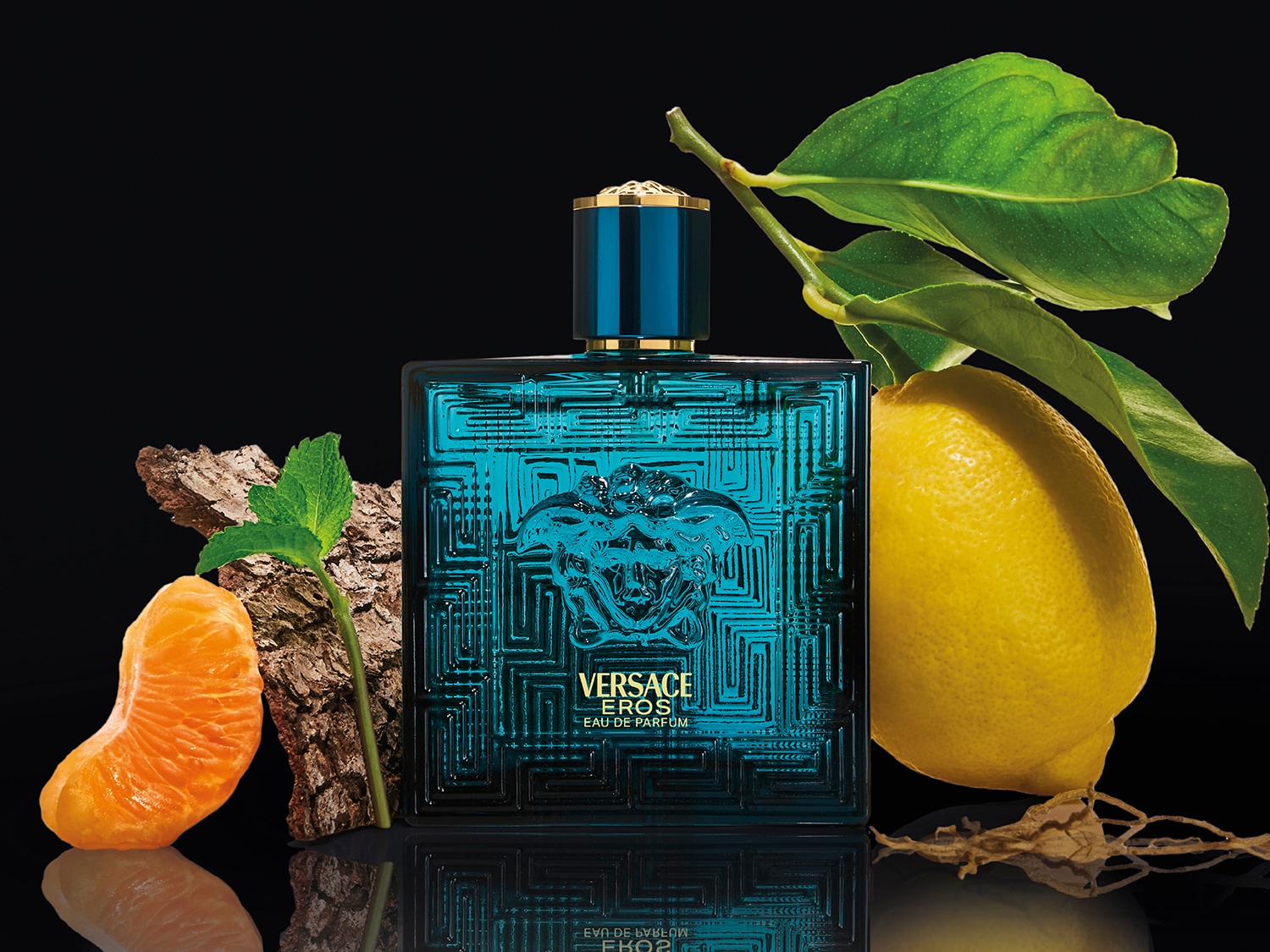 Butelka perfum Versace Eros Parfum w turkusowym szkle z greckim wzorem, otoczona cytryną i pomarańczą na czarnym tle, emanuje świeżością i luksusem.
