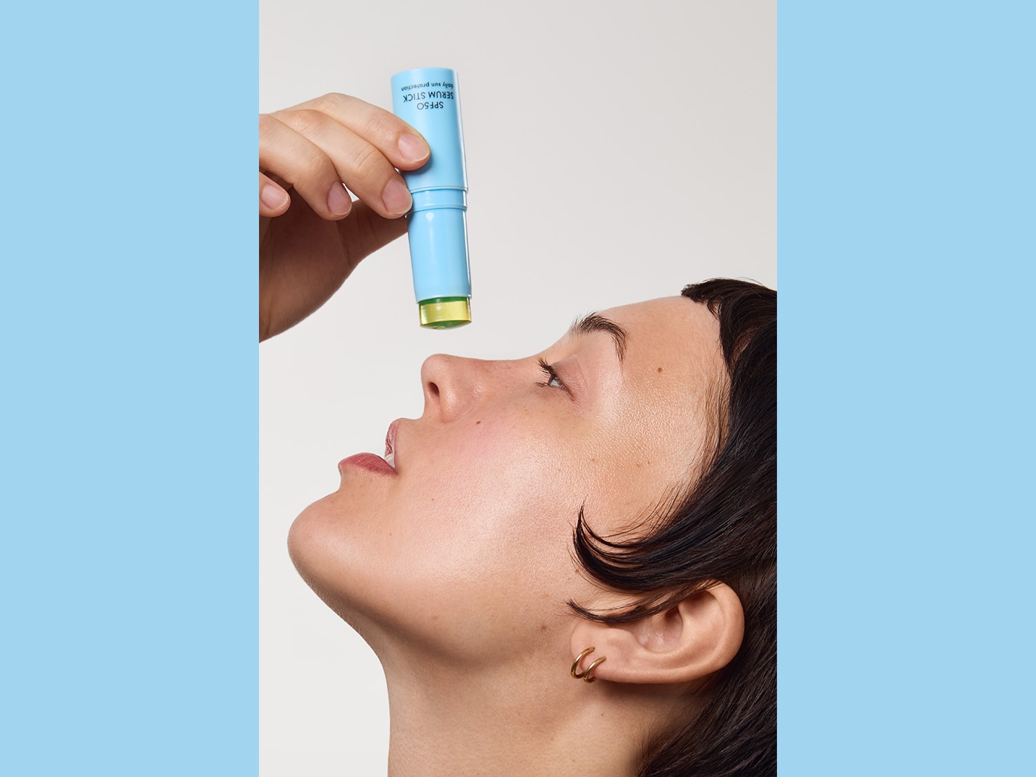 Eine Frau trägt einen SPF50 Serum Stick mit hellblauer Verpackung auf ihre Nase auf, um ihre Haut vor der Sonne zu schützen.