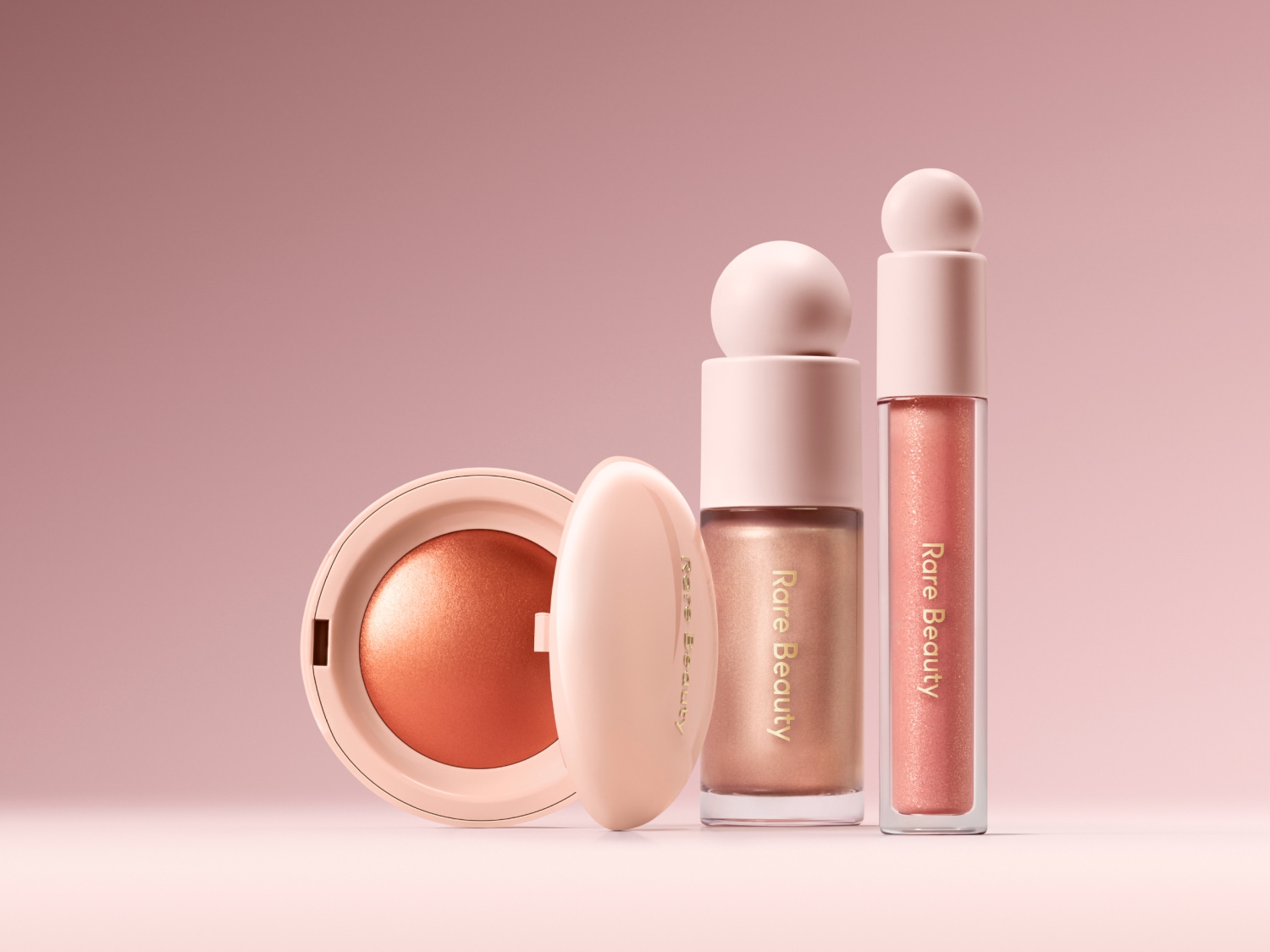 Eine Kollektion von Rare Beauty Make-up-Produkten in Pfirsichfarben, darunter ein Rouge, ein flüssiger Highlighter und ein Lipgloss, die einen sanften, strahlenden Look versprechen.