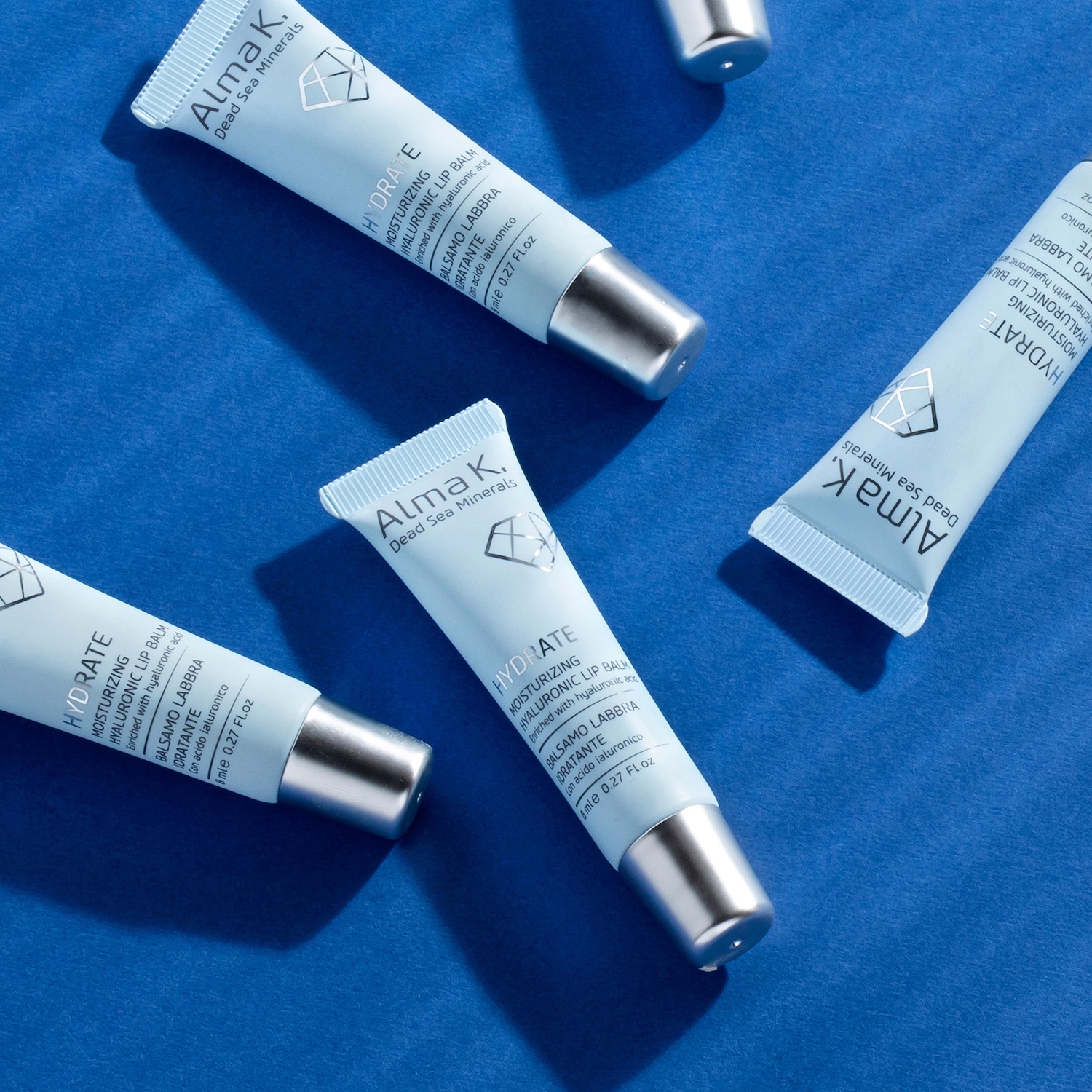 Diversi tubetti di balsamo labbra idratante Alma K. Dead Sea Minerals, con tappi argentati e confezioni azzurre, promettono labbra morbide grazie all'acido ialuronico.