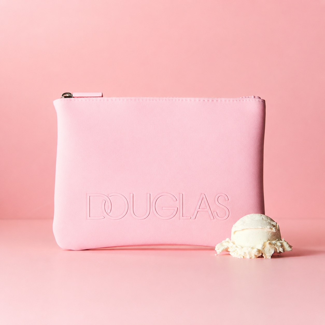 Auf einem rosa Hintergrund ist eine rosa Kosmetiktasche mit dem Douglas-Logo und einer Kugel Eiscreme zu sehen.