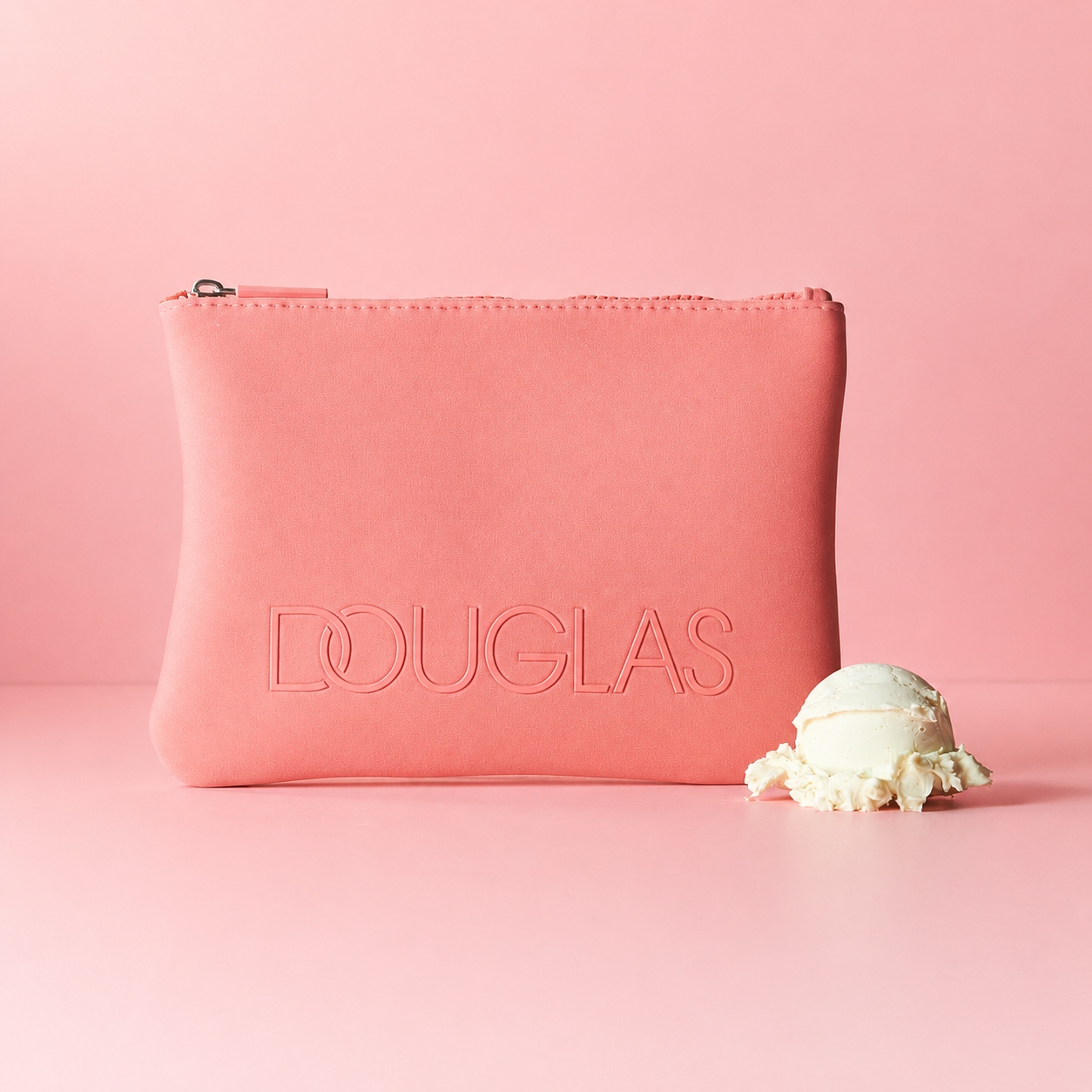 Auf einem rosa Hintergrund befindet sich eine Douglas Kosmetiktasche in Rosa mit einem Eis.