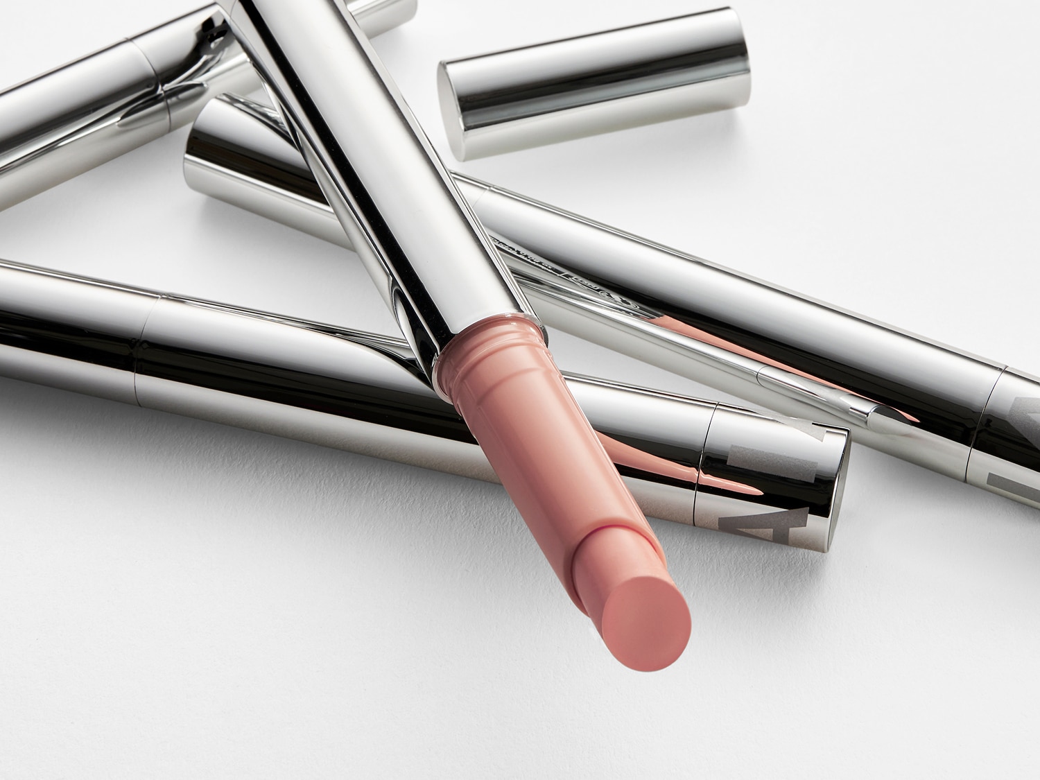 Nahaufnahme von mehreren silbernen Lippenstiften, einer davon mit einer hellrosa Farbe, die die Textur und den Farbton des Produkts hervorhebt.