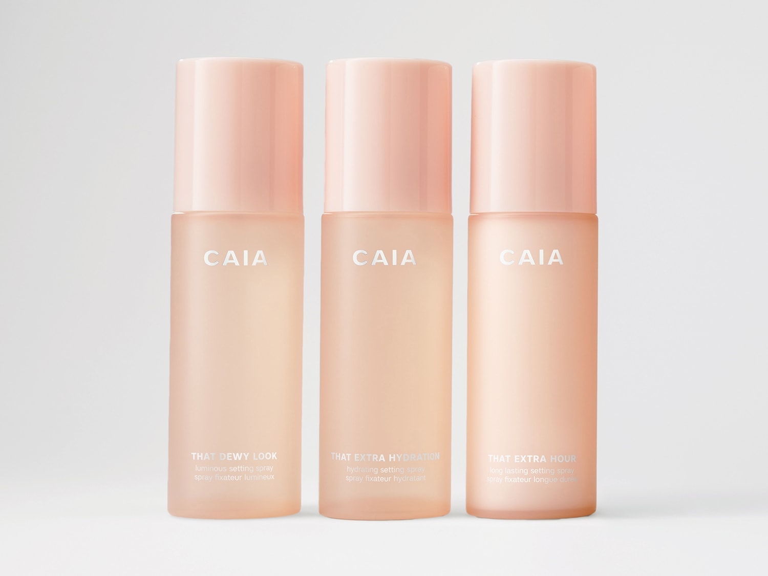 Drei Sprays von CAIA in pfirsichfarbenen Verpackungen: That Dewy Look für einen strahlenden Teint, That Extra Hydration für Feuchtigkeit und That Extra Hour für langanhaltendes Make-up.