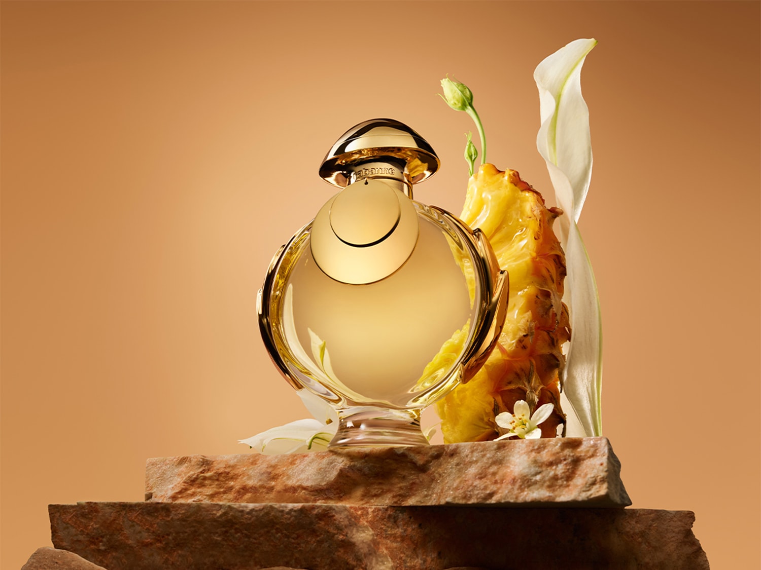Découvrez le parfum doré dans un flacon rond, posé sur une pierre avec des fleurs blanches et un ananas, évoquant un parfum tropical et luxueux.