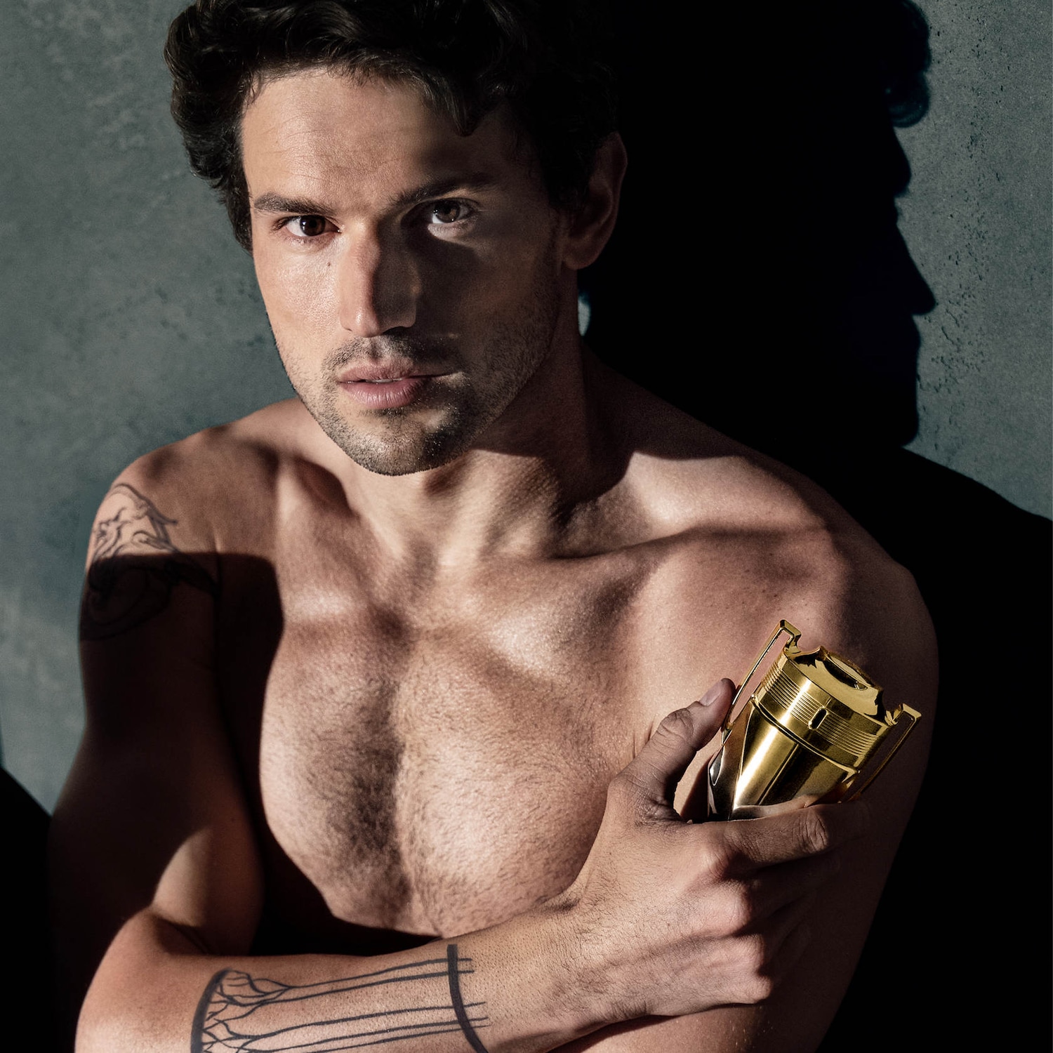 Un homme torse nu, le regard intense, tient un trophée doré, symbole de victoire et de parfum.