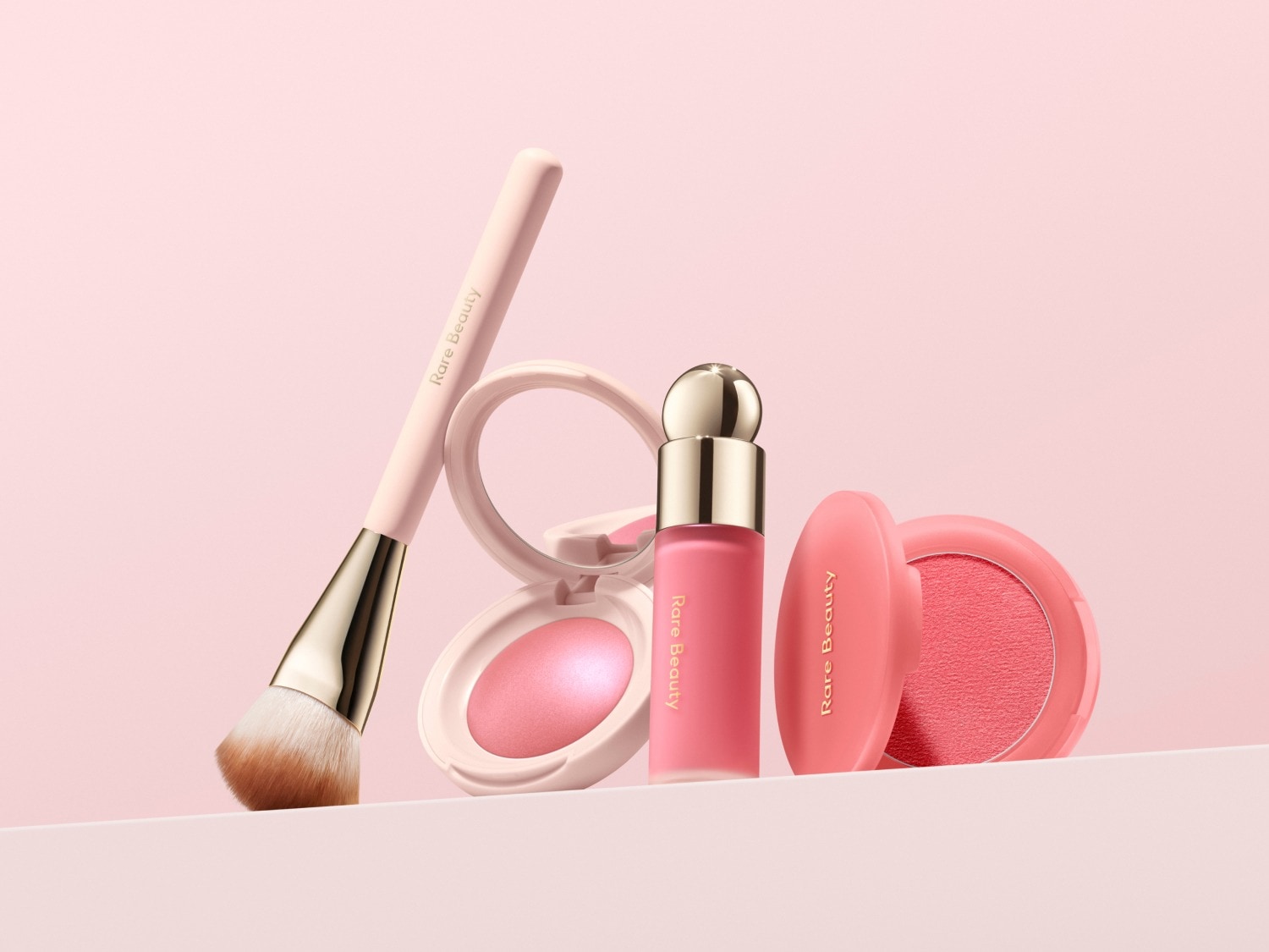 Roze Rare Beauty make-up collectie met een blush kwast, een vloeibare blush met een gouden dop en een compacte blush.