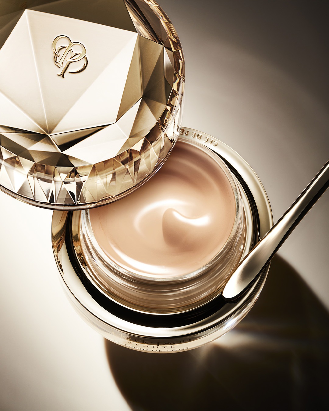 Nahaufnahme einer luxuriösen goldenen Dose mit einer beigen Creme und einem goldenen Spatel, die die reichhaltige Textur und die elegante Verpackung des Produkts hervorhebt.