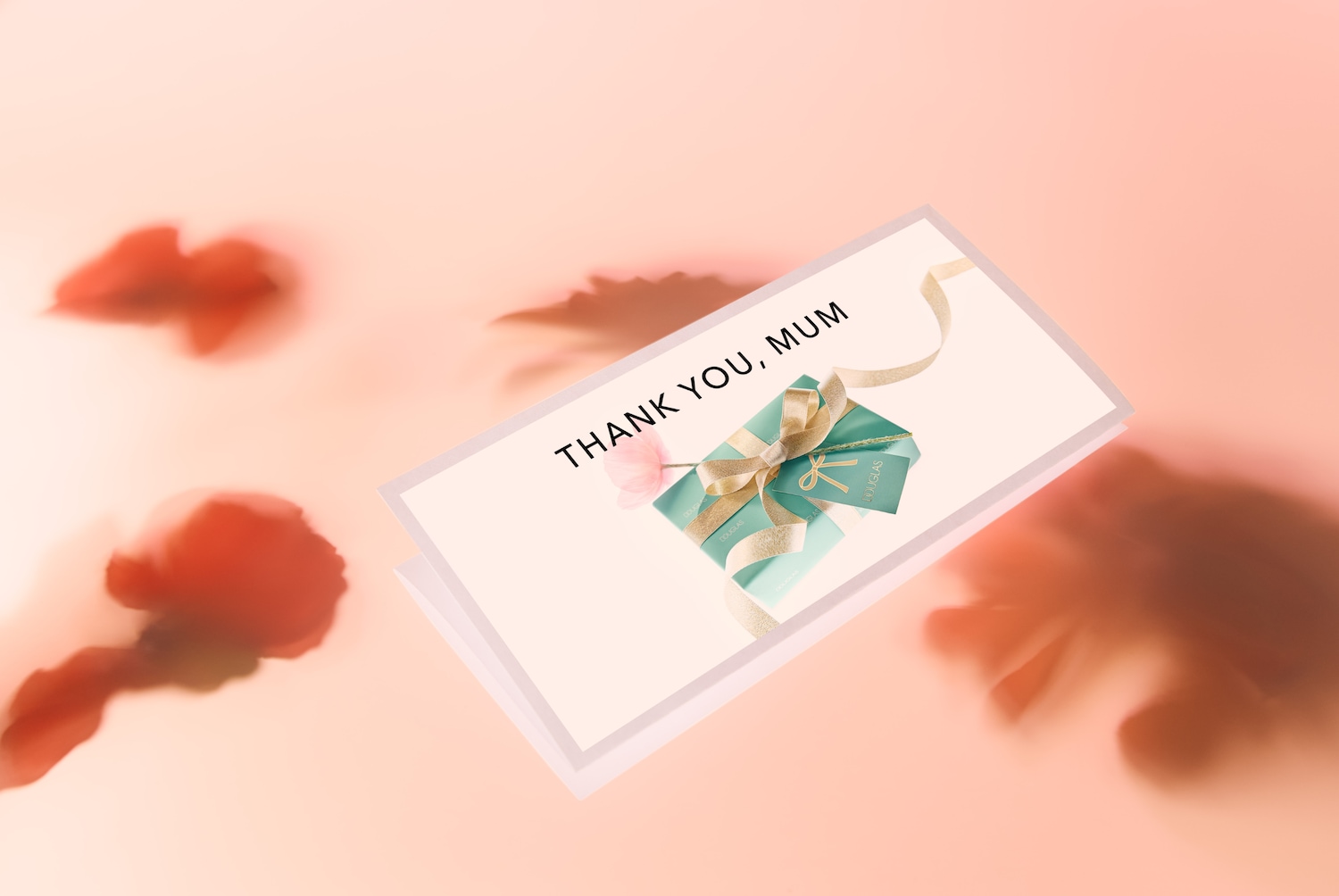 Pohlednice s nápisem „Děkuji, mami“ s dárkem Douglas zabaleným ve světle modrém papíru a zlatou stuhou, doplněná malou růžovou květinou.