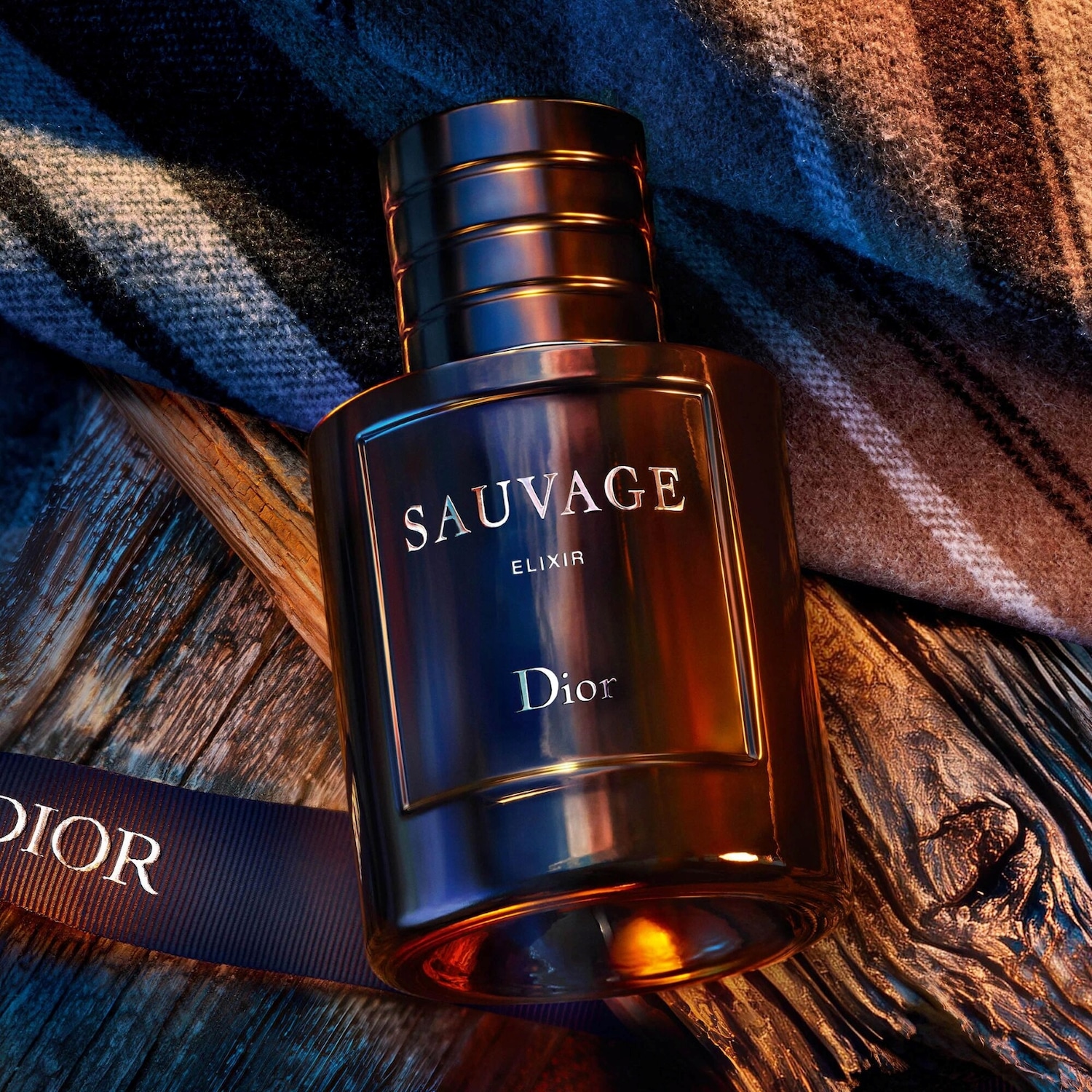 Découvrez Sauvage Elixir de Dior, un parfum intense dans un flacon élégant aux reflets dorés, posé sur du bois texturé et un ruban bleu marine portant le nom Dior.