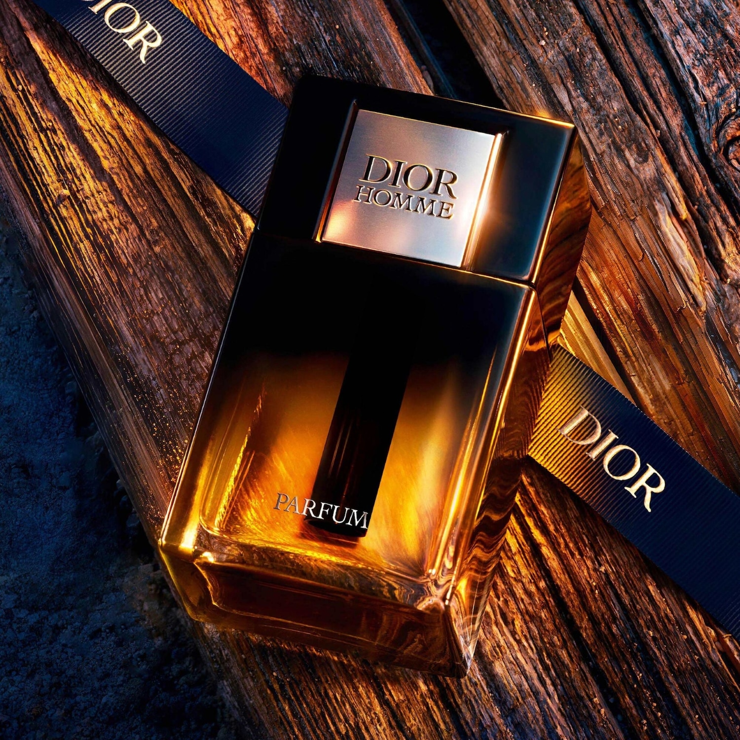 Découvrez Dior Homme Parfum, un parfum ambré boisé intense dans un flacon élégant, posé sur un ruban Dior bleu marine.
