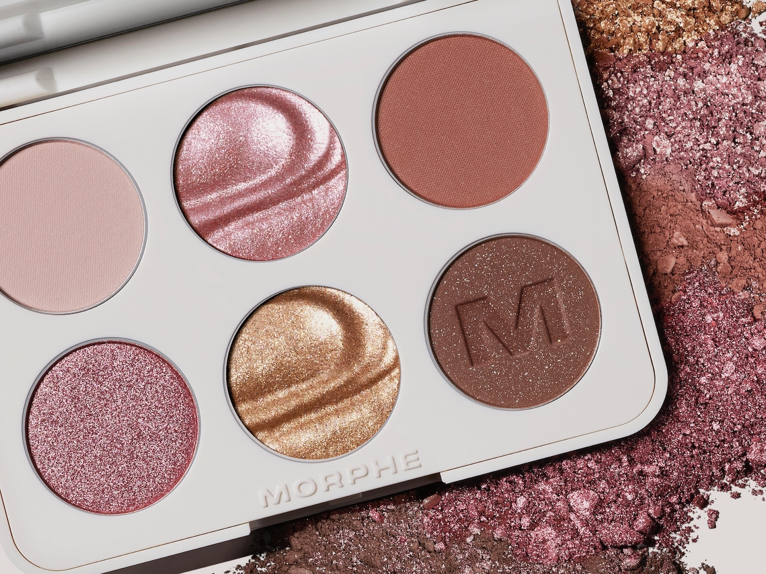 Nahaufnahme einer Palette von Morphe mit sechs runden Farbtönen in Rosa-, Gold- und Brauntönen, einige mit Schimmer, in einer weißen Kompakthülle.