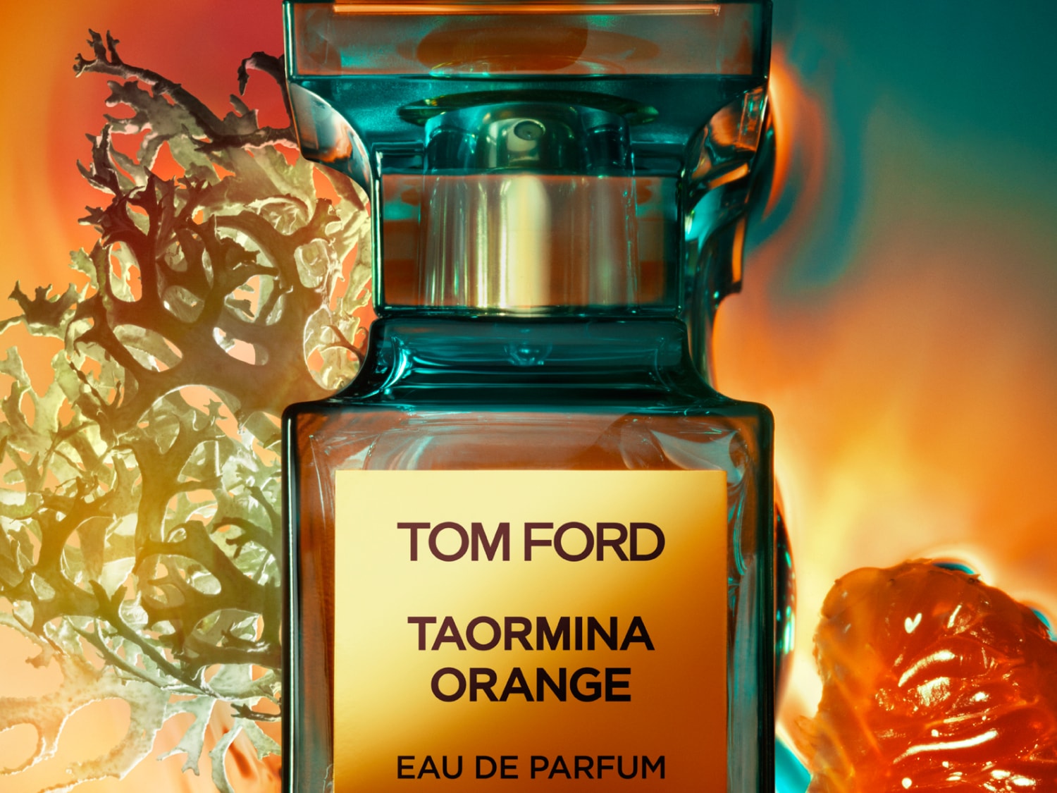 Butelka perfum Tom Ford Taormina Orange Eau de Parfum o pojemności 50 ml ma przezroczystą, kwadratową butelkę z pomarańczową etykietą i turkusową nakrętką, otoczoną suszonymi roślinami i pomarańczą.