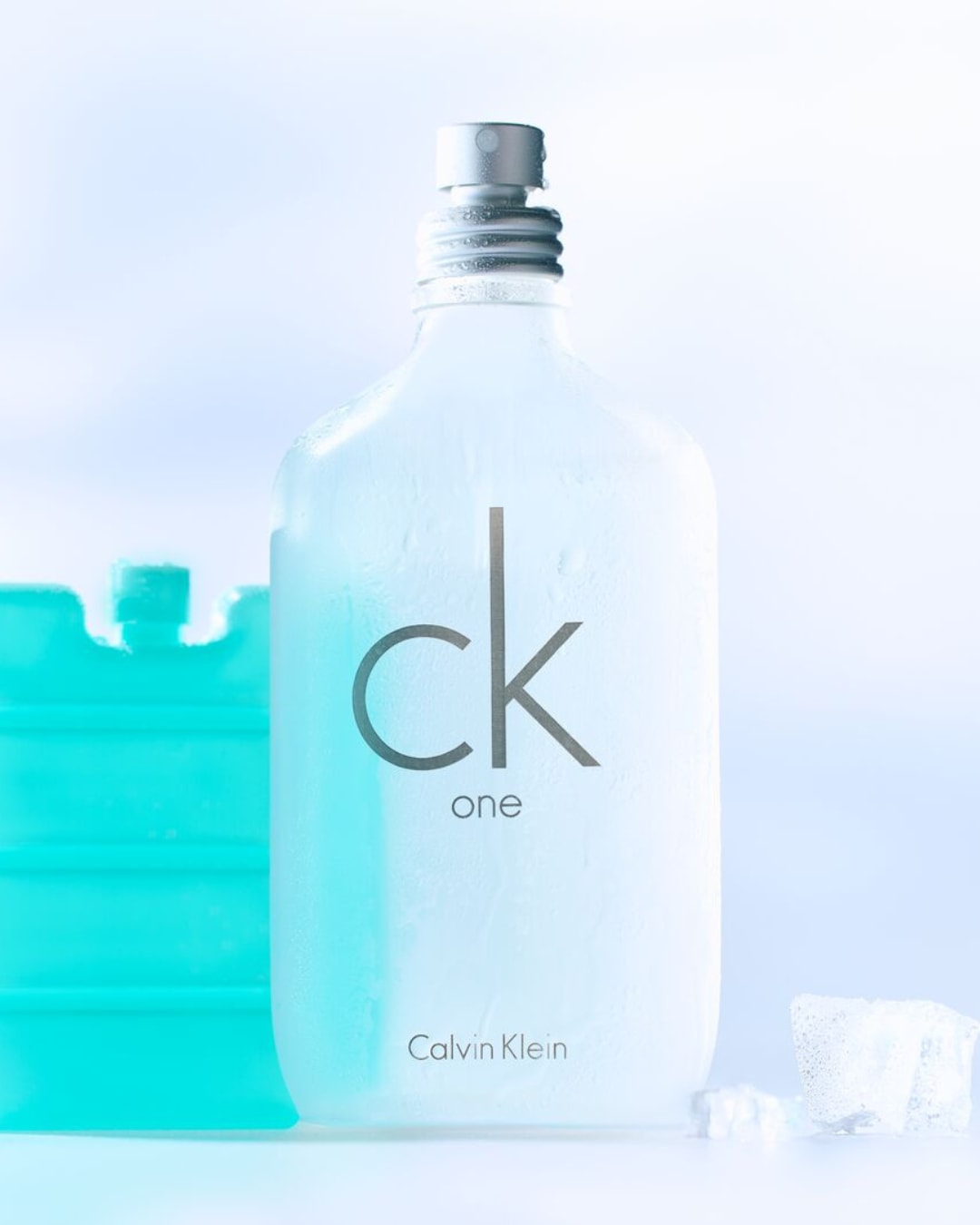 Een bevroren fles Calvin Klein CK One-parfum staat naast een blauw koelelement en ijsblokjes, wat de frisse geur van het parfum benadrukt.