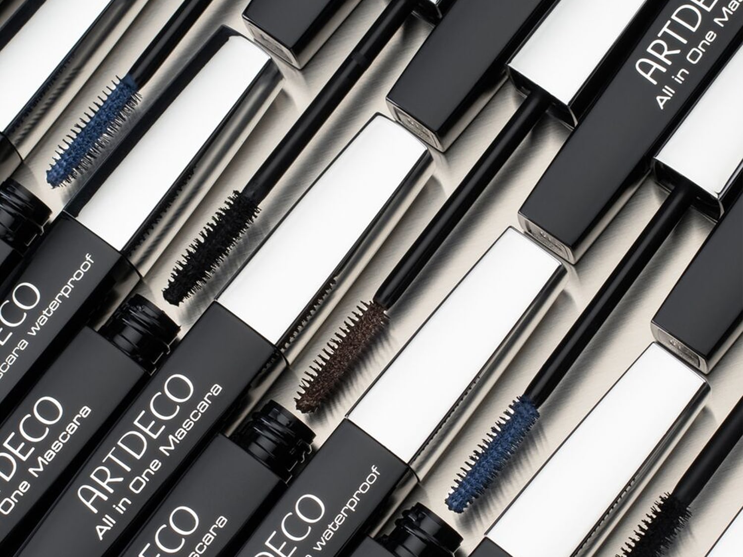 Mehrere geöffnete Tuben ARTDECO All in One Mascara in Blau, Braun und Schwarz liegen nebeneinander auf hellem Untergrund.