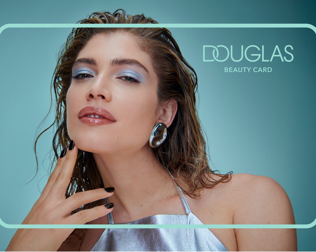 Portrét ženy s modrými očními stíny a lesklými rty, na sobě má stříbrný top a velké náušnice, v pozadí logo Douglas Beauty Card.